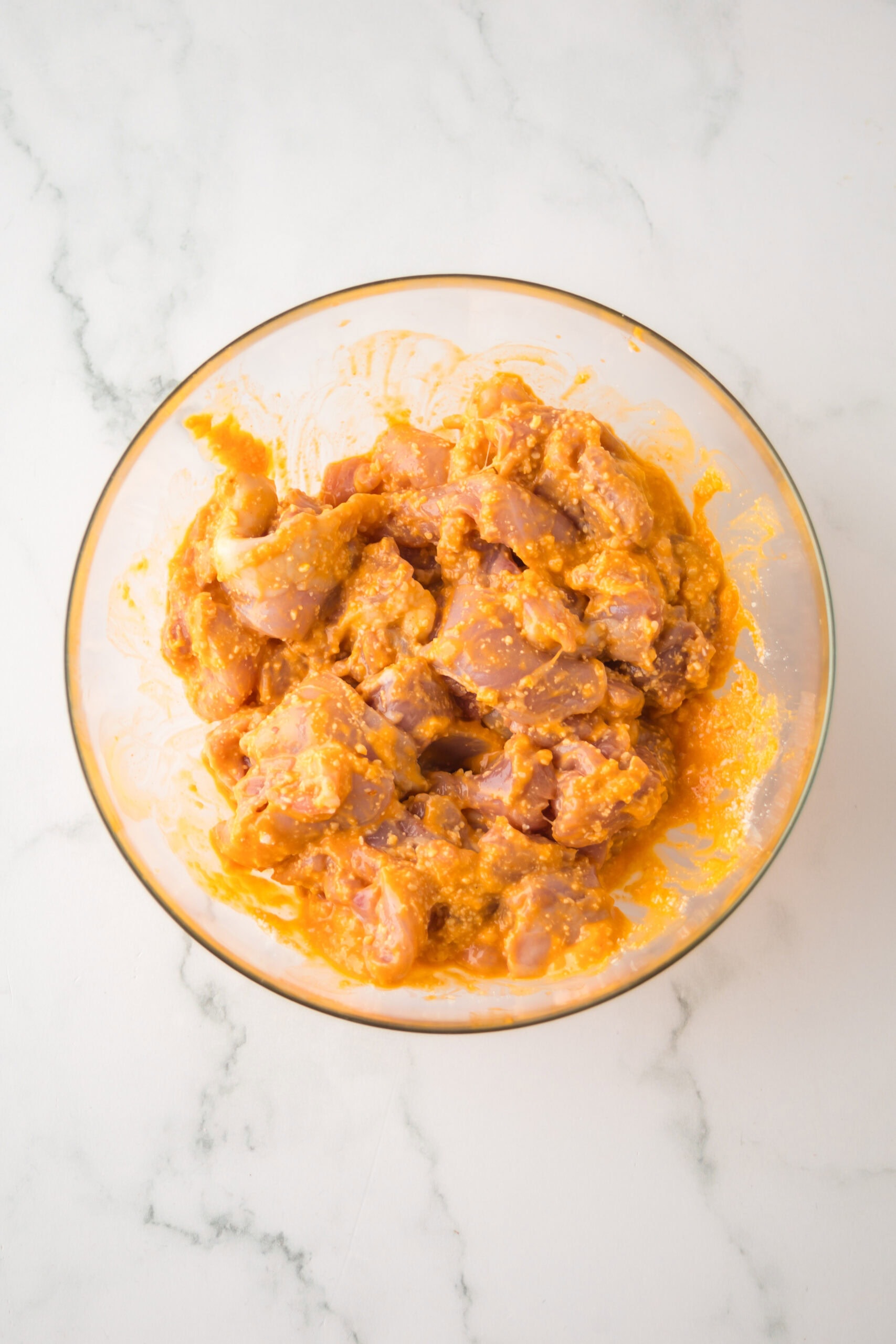 Chicken thighs in a bowl, with parmesan cheese and buffalo sauce, all mixed together