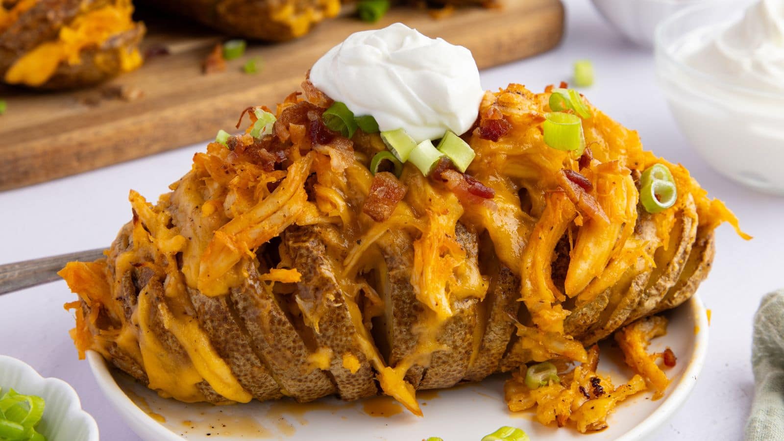 a close up of buffalo chicken stuffed potatoes topped with crumbled bacon, green onions, and sour cream