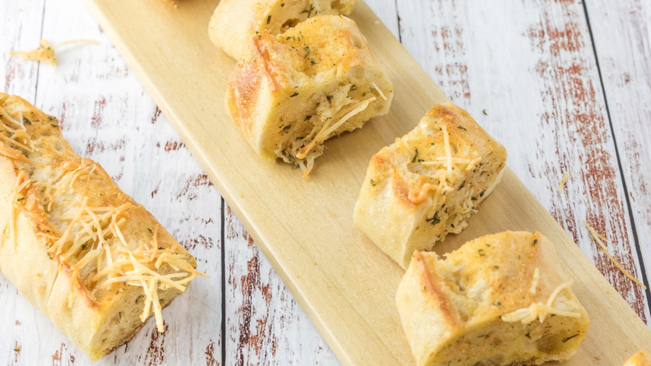 Cheesy garlic bread that is cut into slices on a wooden cutting board, and ready to be enjoyed