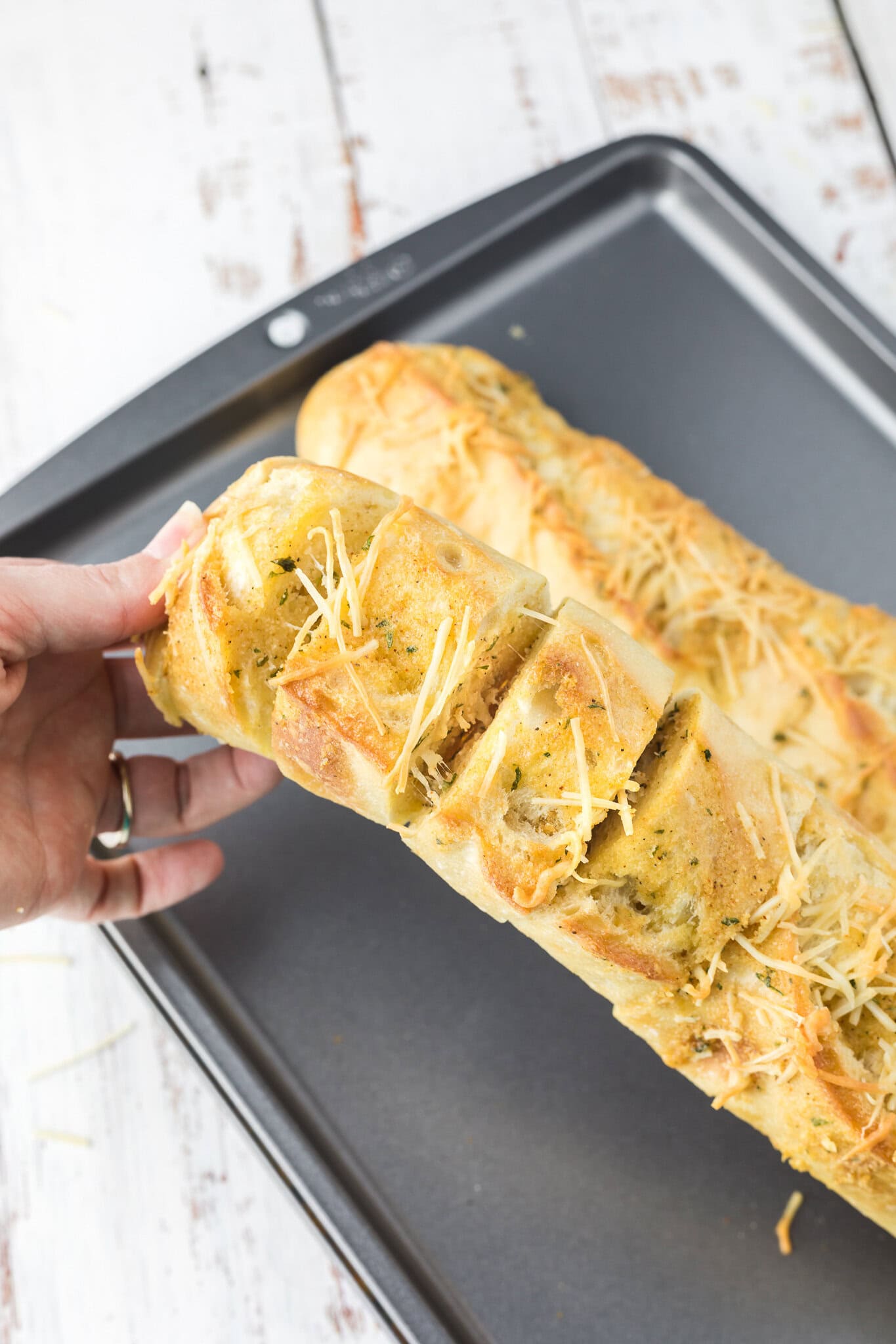 Cheesy garlic bread all baked and cut into slices, a hand is holding the bread to showing its texture inside