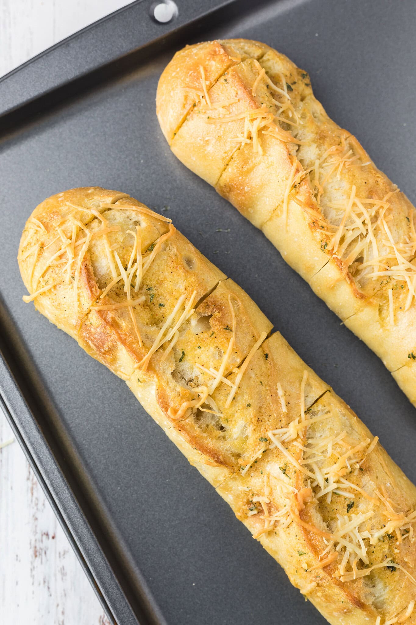 Cheesy garlic bread is cut into slices on a baking sheet, all baked