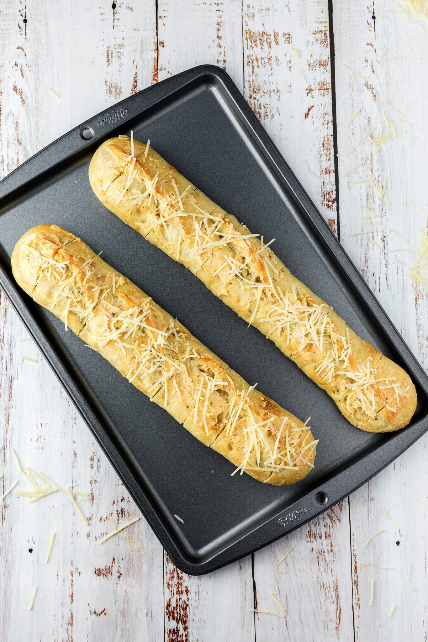 Parmesan cheese on top of sliced cheesy bread on a baking sheet