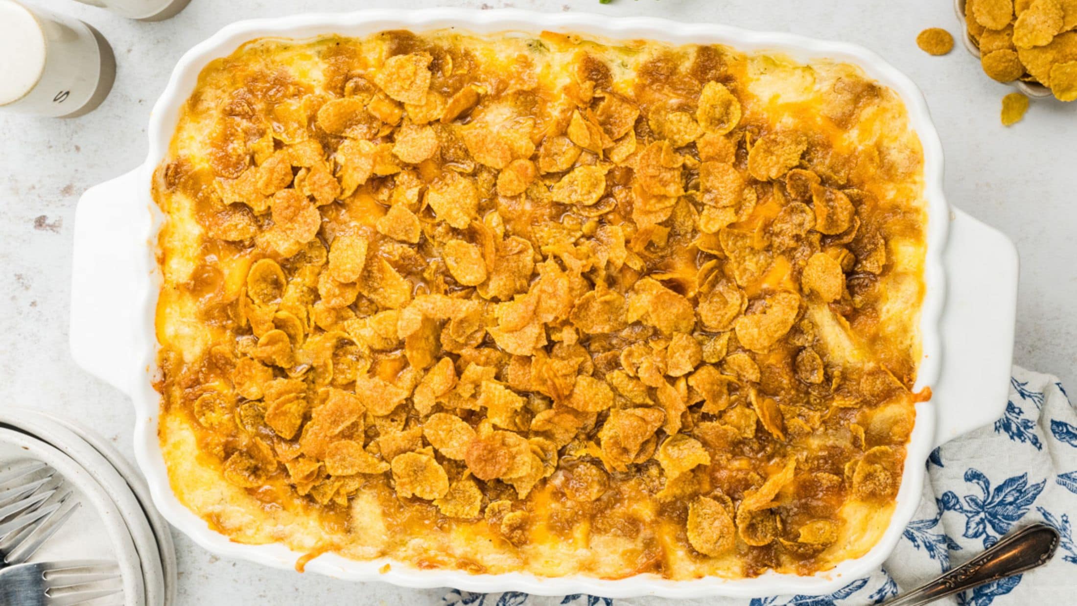 Full baking dish with baked cheesy potatoes, bowls and forks on the side to be ready to serve it