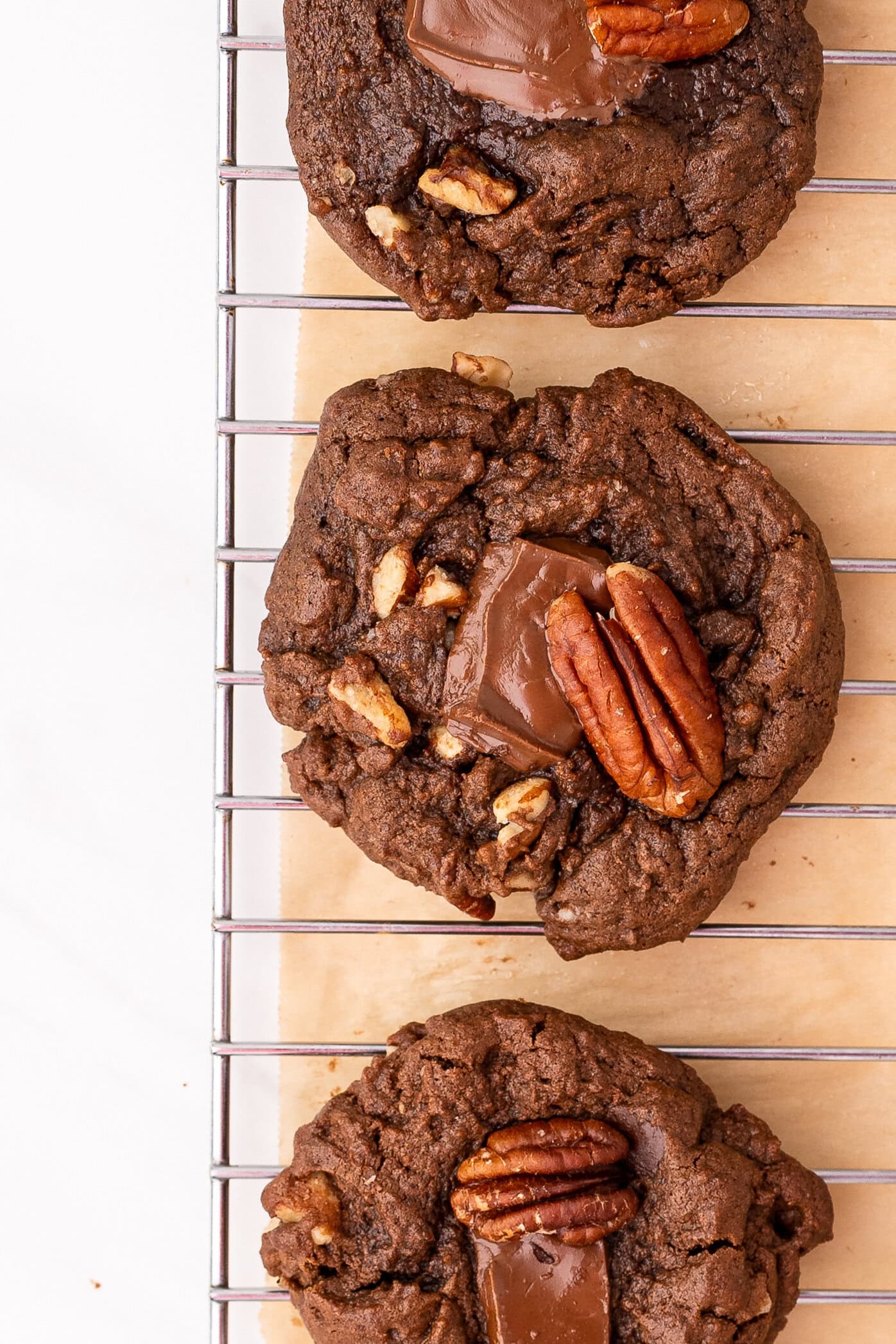 Three double chocolate pecan cookies on a wire rack