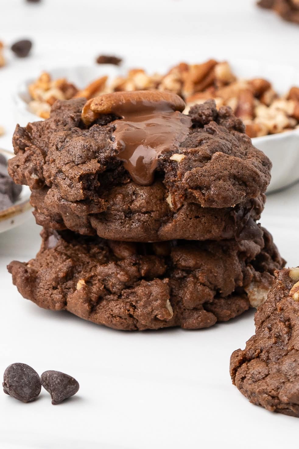 A stack of chewy double chocolate pecan cookies, melted chocolate bar on top of the top cookie of the stack
