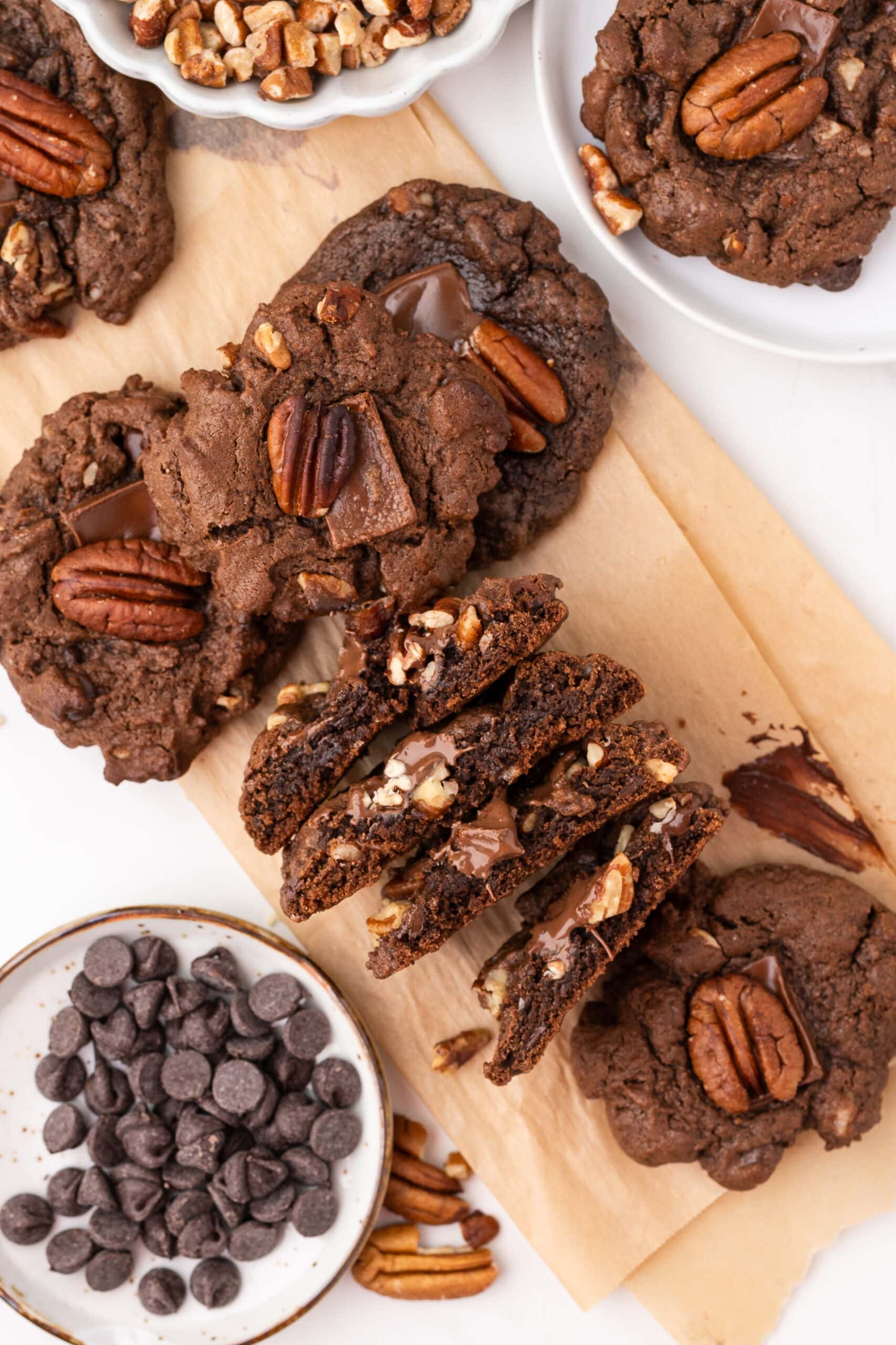 Chewy double chocolate pecan cookies all stacked and a few are cut in half to see the inside texture of the cookies
