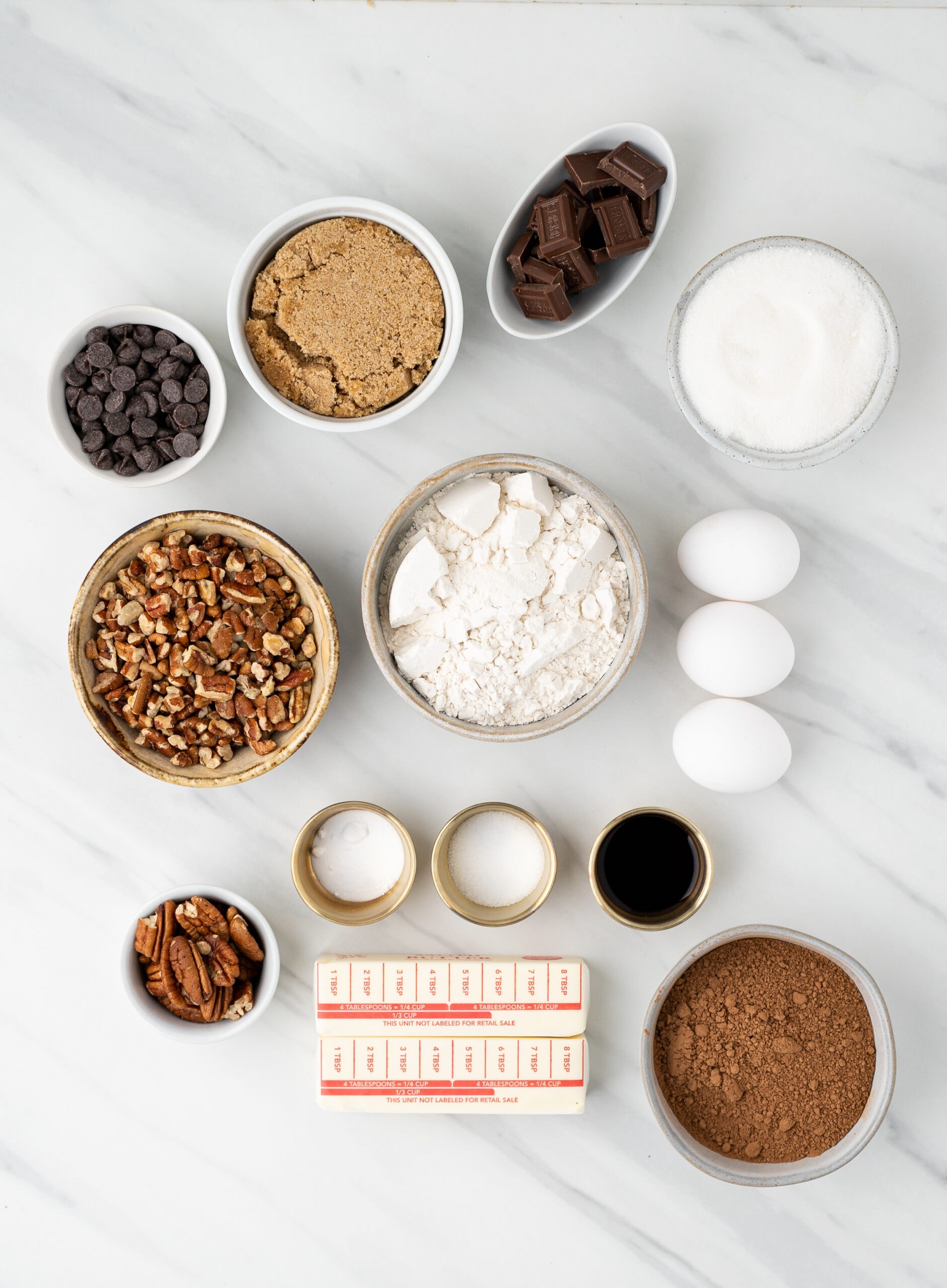 Ingredients to make chewy double chocolate cookies: butter, brown and white sugar, vanilla, eggs, cocoa powder, flour, baking soda, salt, chocolate chips, pecans. dark chocolate bars
