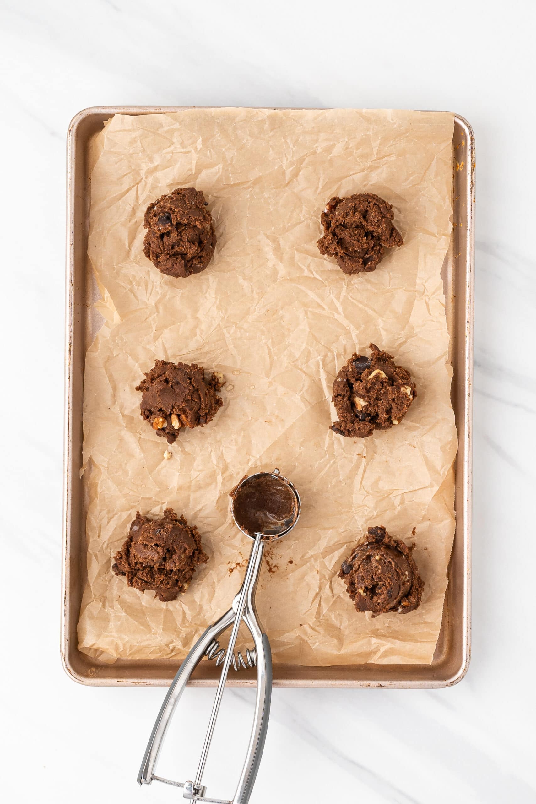 Chewy chocolate cookie dough all mixed and scooped out using a scooper to make the same size cookies. They are being placed on a baking sheet with parchment paper