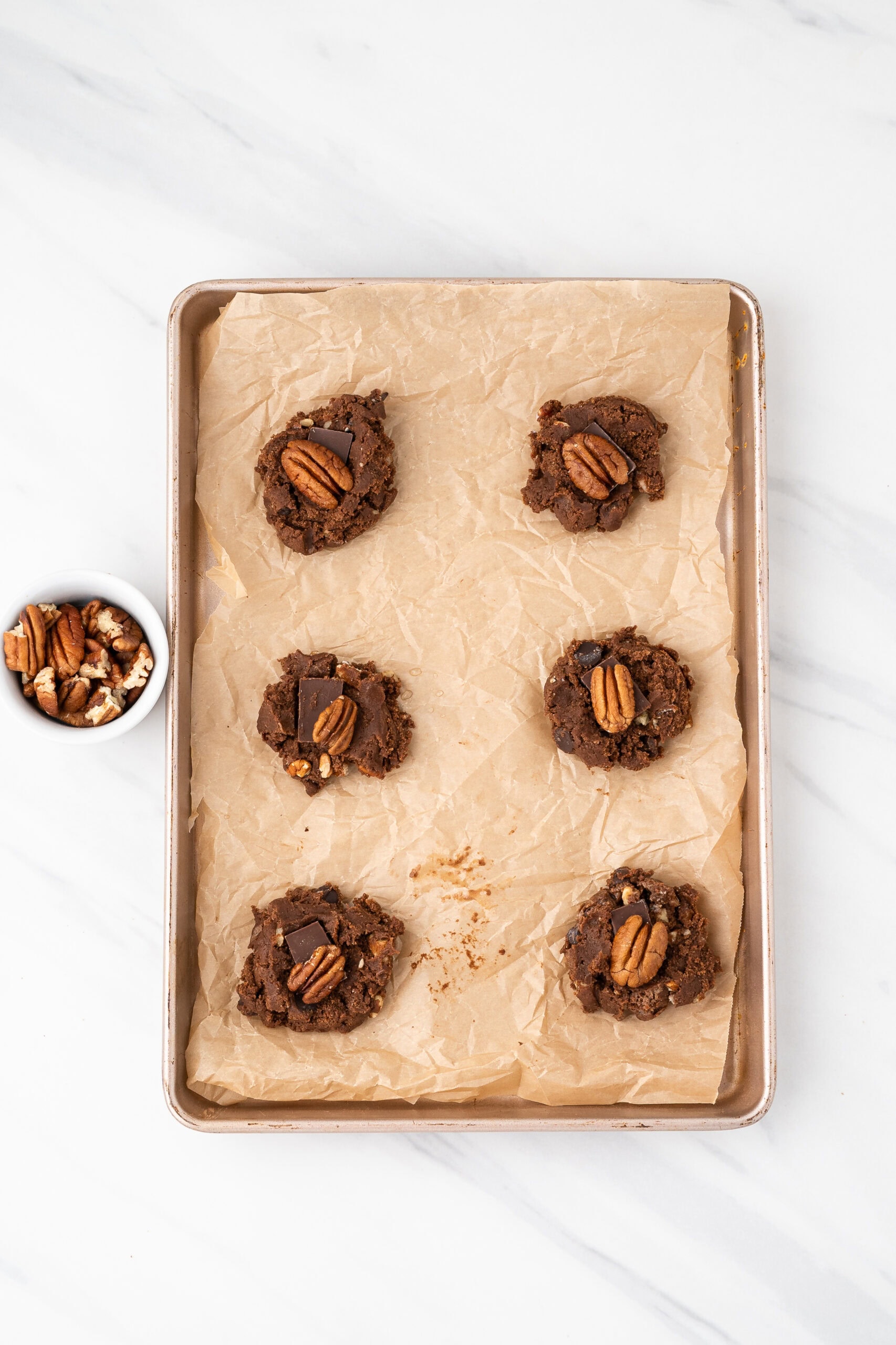 Pecan and chocolate bar being added on top of the chocolate dough cookies