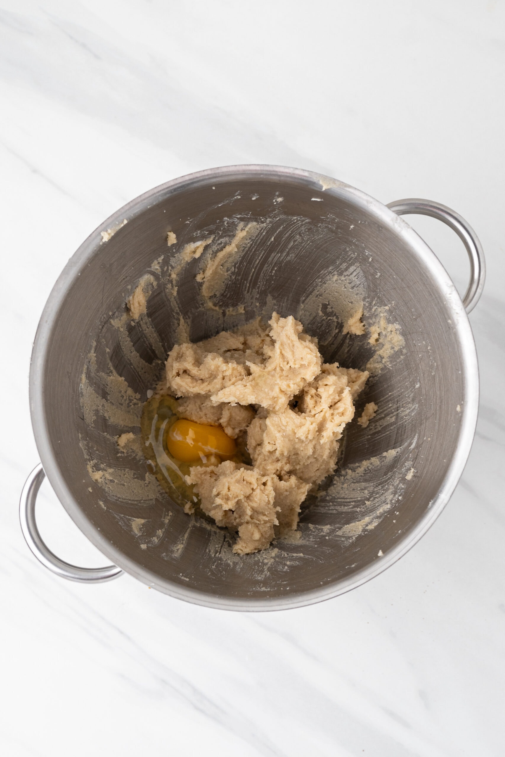 Adding an egg to the butter and sugar mixture in a bowl
