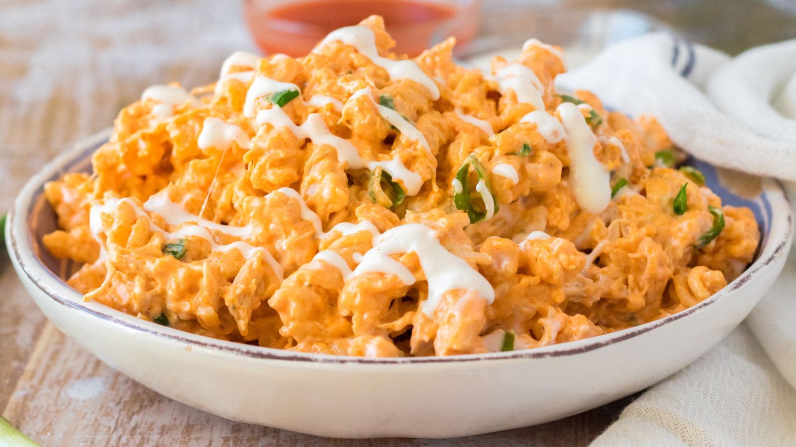 a close up of crockpot buffalo chicken mac and cheese drizzled with ranch dressing in a white bowl