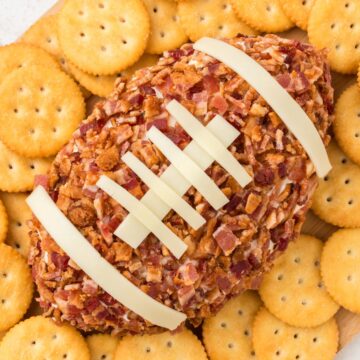a close up of jalapeno popper football cheeseball covered in bacon and surrounded by Ritz crackers