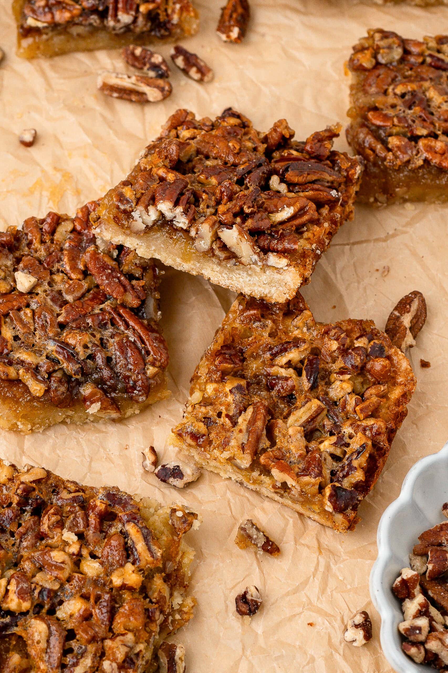 Pecan pie bars all baked on parchment paper, chopped pecans all around