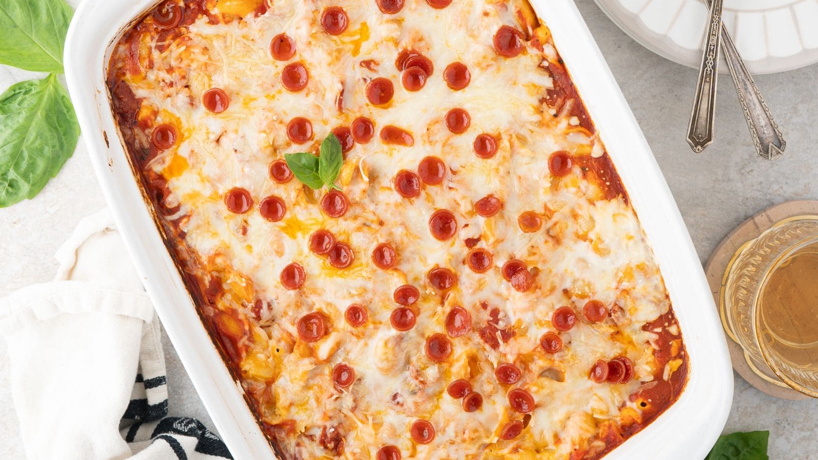 a close up of pepperoni pizza mac and cheese topped with melty mozzarella and mini pepperoni in a white baking dish