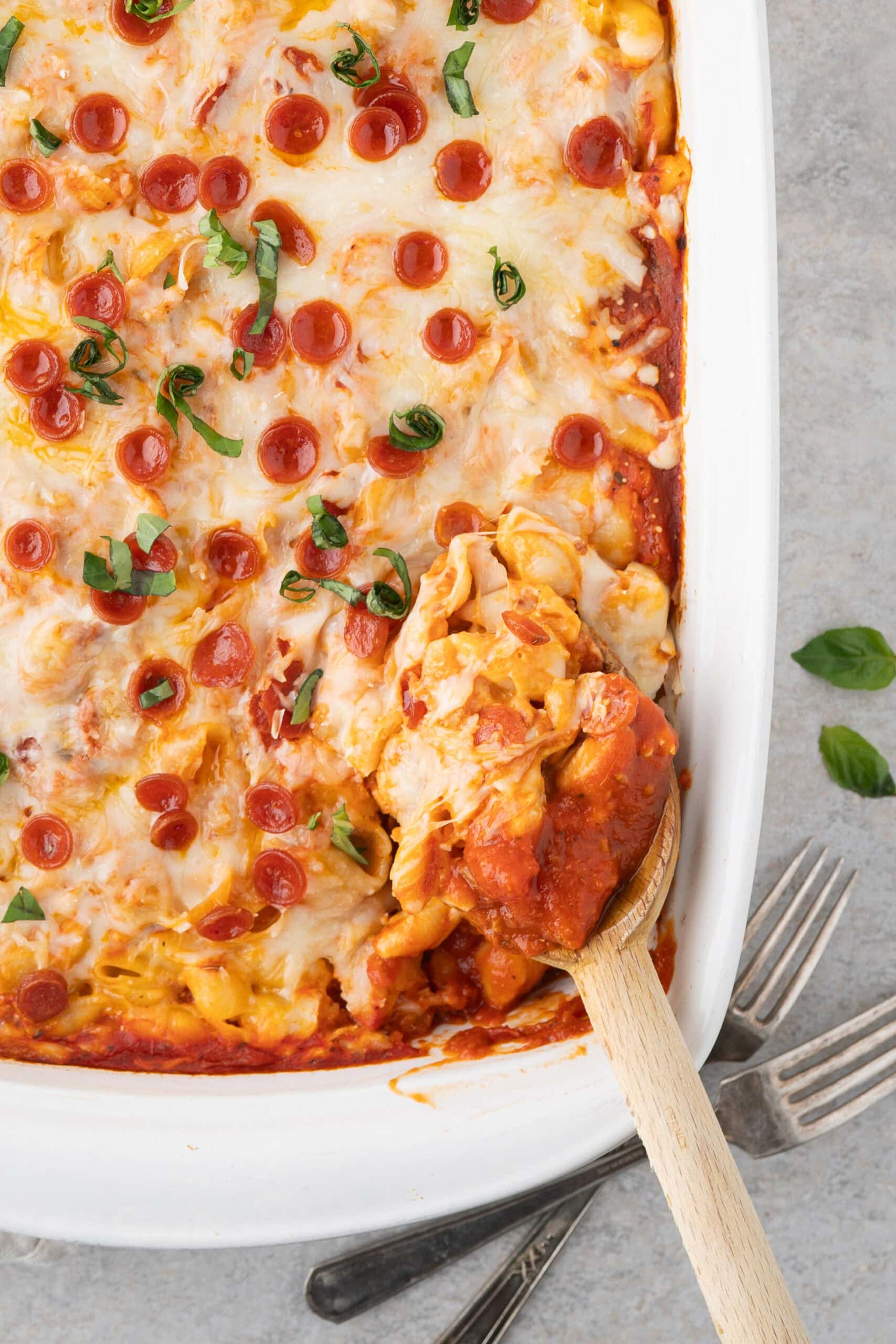 A wooden spoon is scooping up pepperoni pizza mac and cheese to be plated