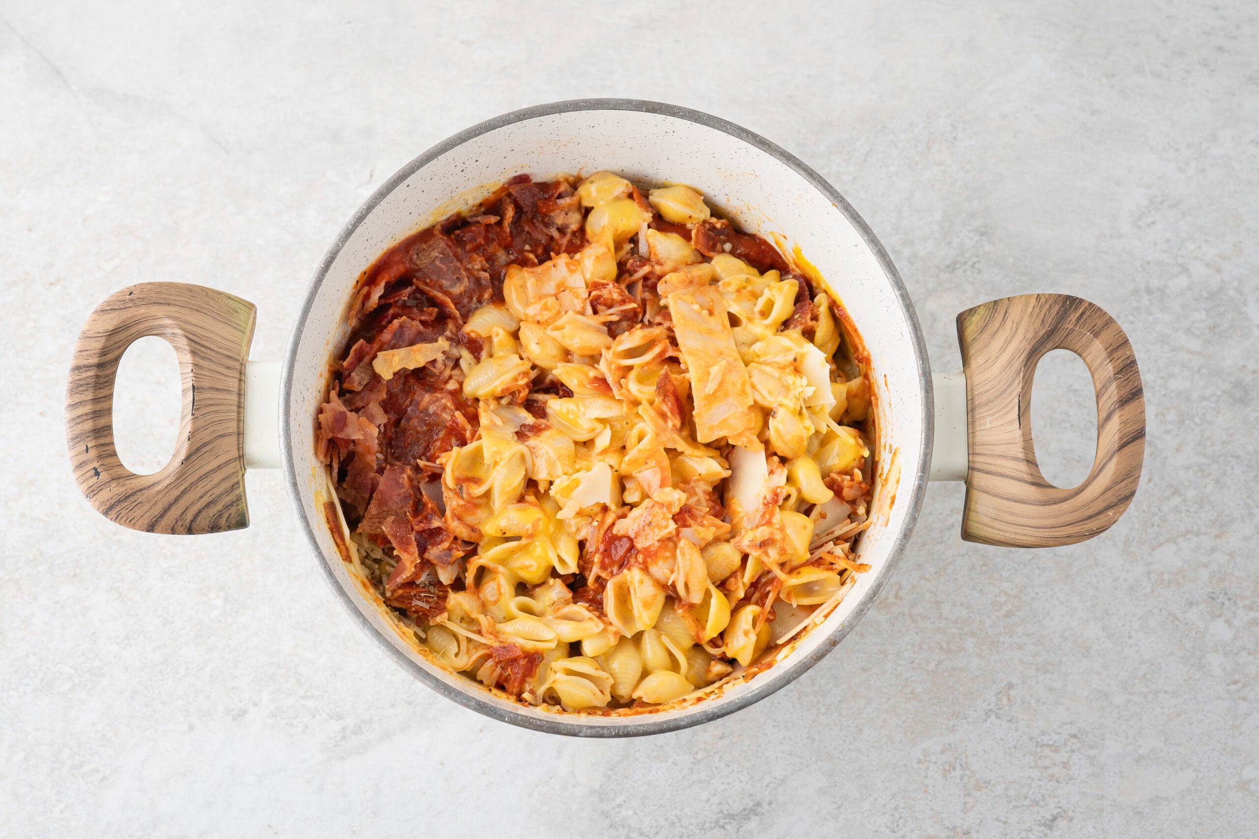 Adding the finished Velvetta pasta and cheese with pizza sauce, bacon, mini pepperoni, cheese, italian seasoning in a saucepot