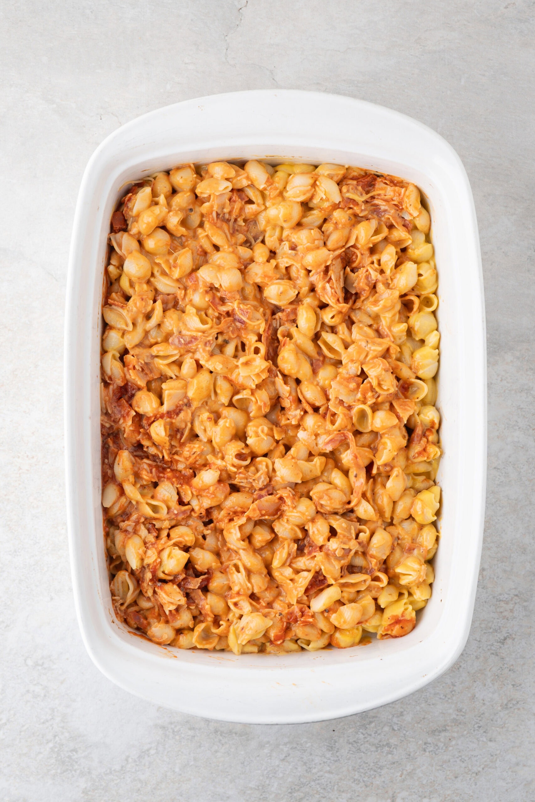 Adding Velvetta pasta and shells to the pizza sauce in a baking dish