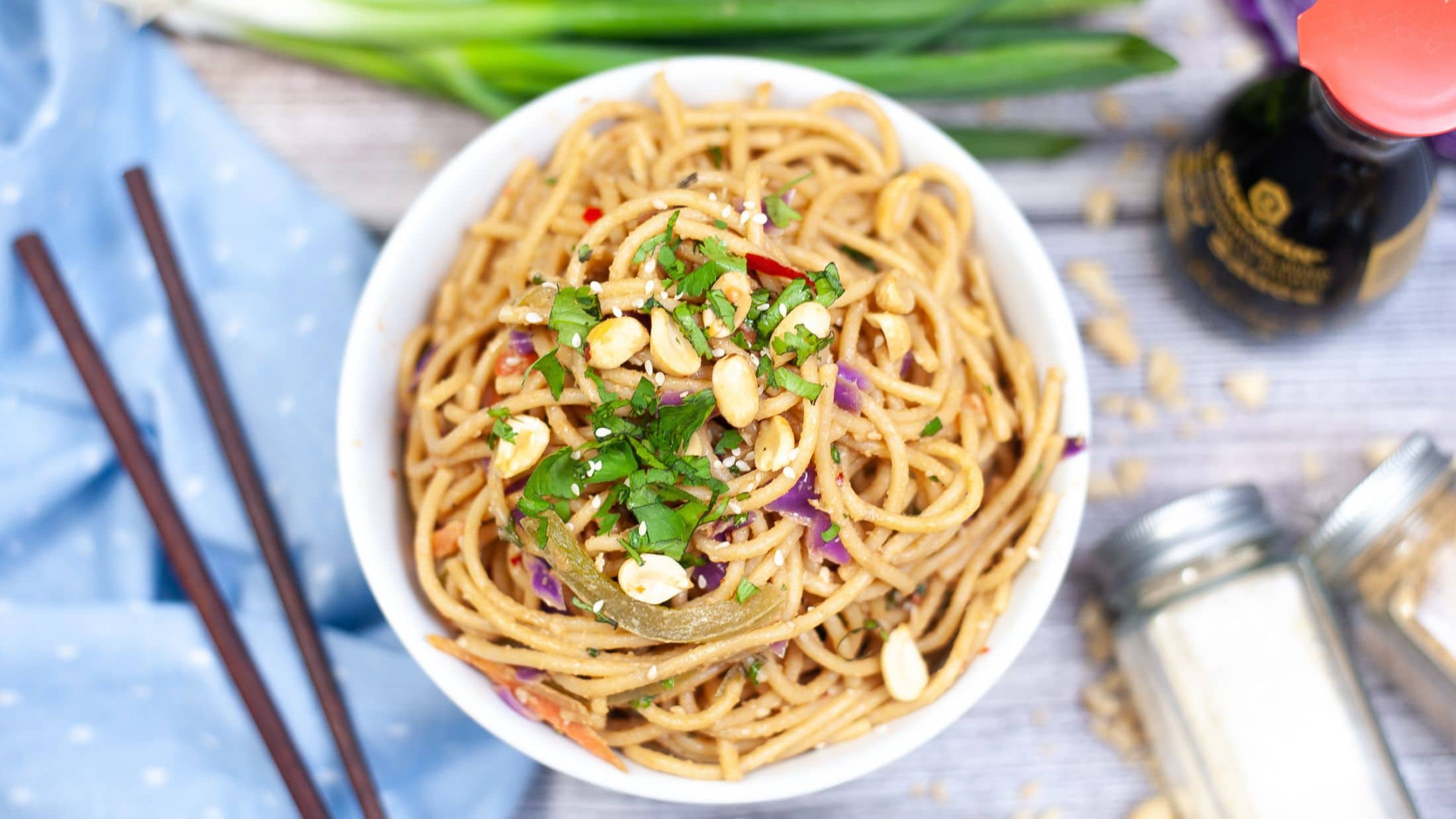 A bowl of spicy Thai peanut noodles with chopsticks to the side