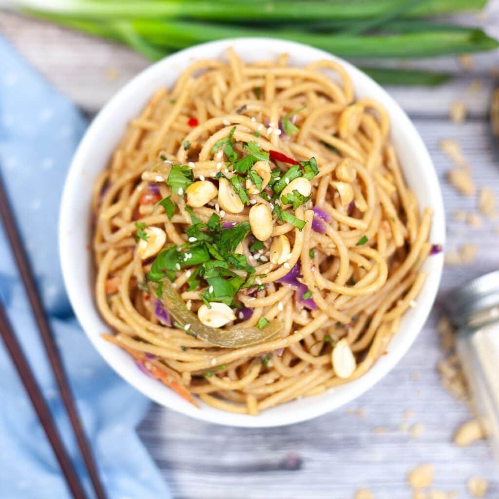 A bowl of Thai peanut noodles in a white bowl served with chopsticks