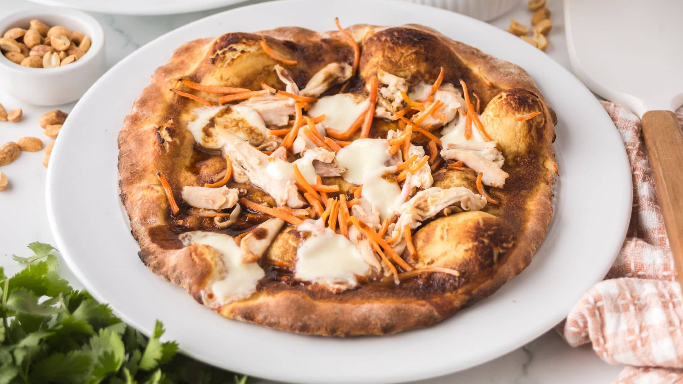 Baked Thai Chicken Pizza on a white plate, surrounded by parsley and peanuts. Ready to be enjoyed