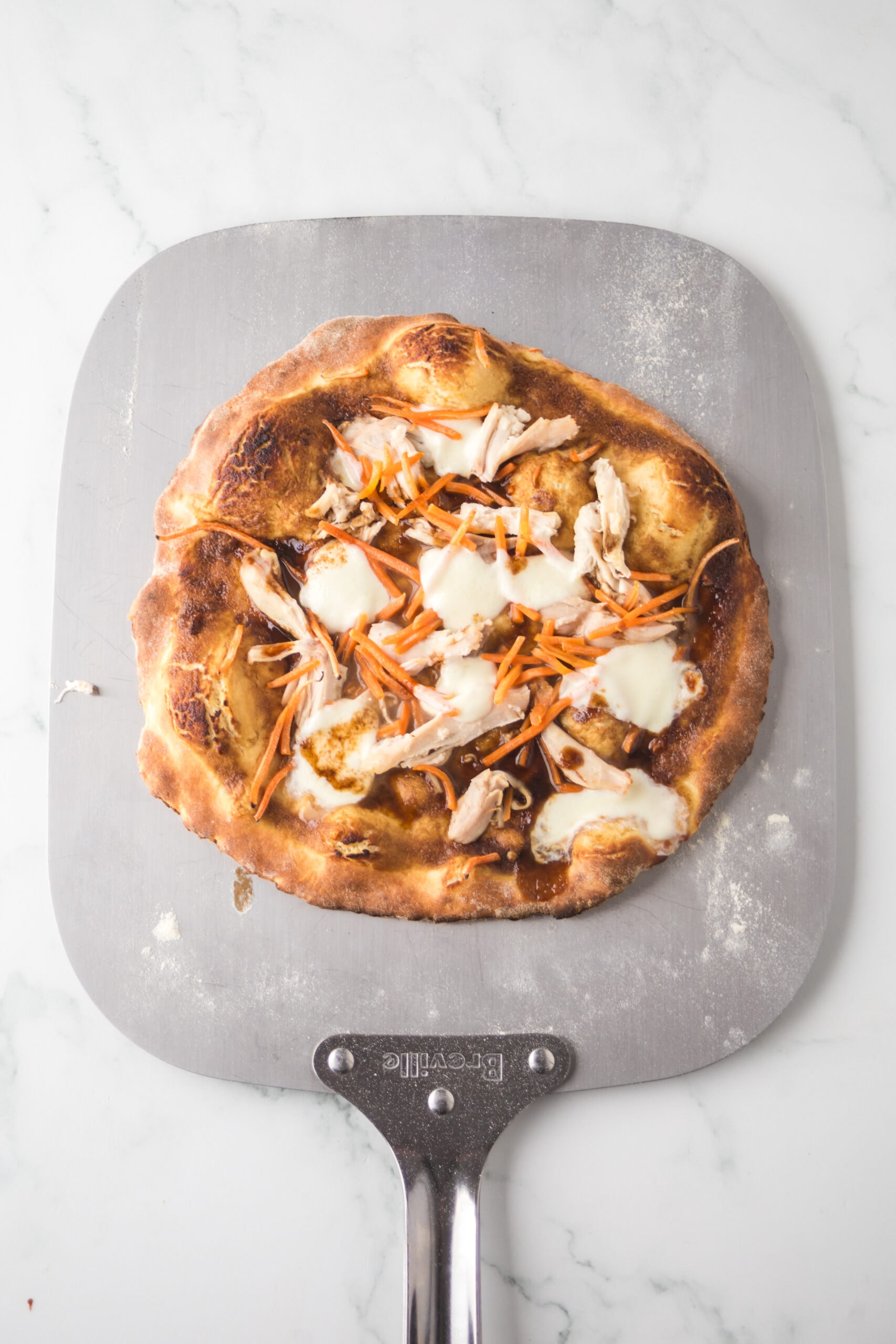 Thai chicken pizza is on a pizza stone, ready to be baked