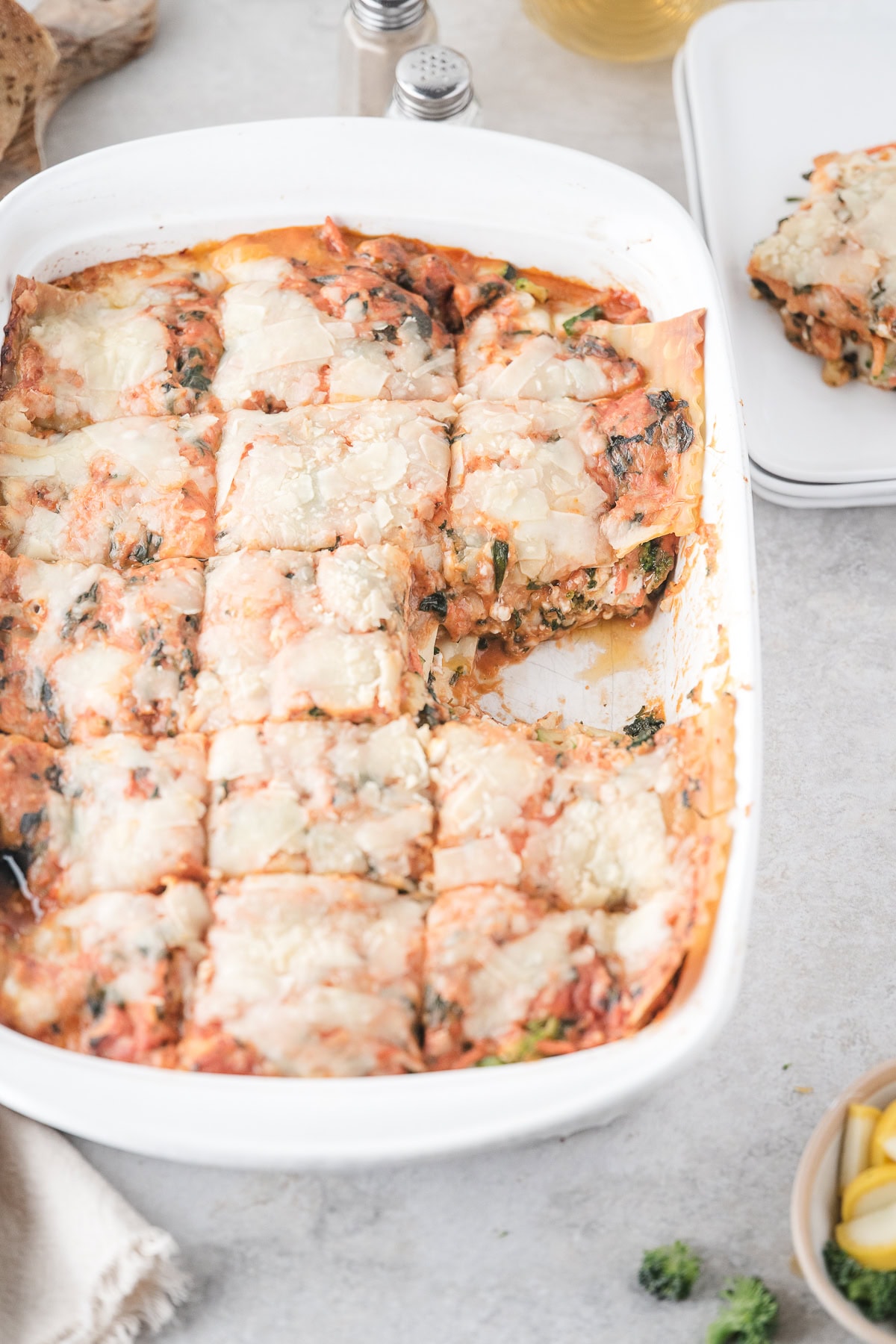 A square piece of veggie lasagna is placed on a plate, and showing the inside of the lasagna in baking pan