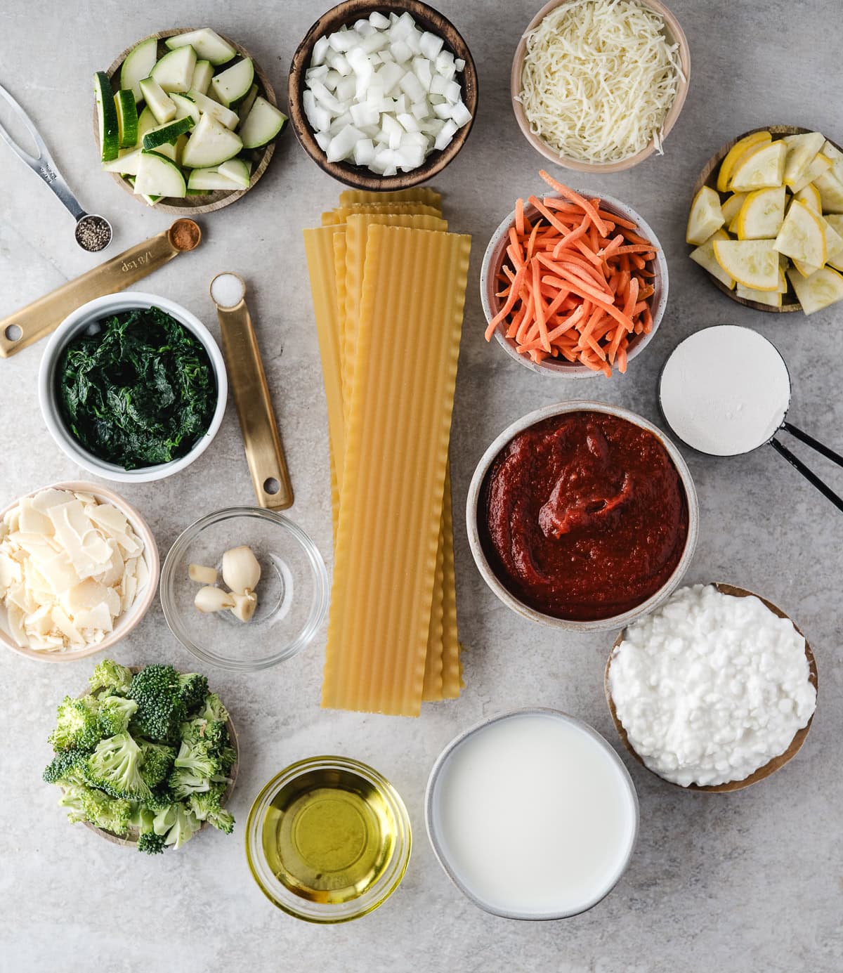 All ingredients pictured: lasagna noodles, onion, garlic, olive oil, zucchini, squash, carrots, broccoli, salt, flour, milk, parmesan cheese, pepper, nutmeg, spaghetti sauce, spinach, cottage cheese, mozzarella cheese