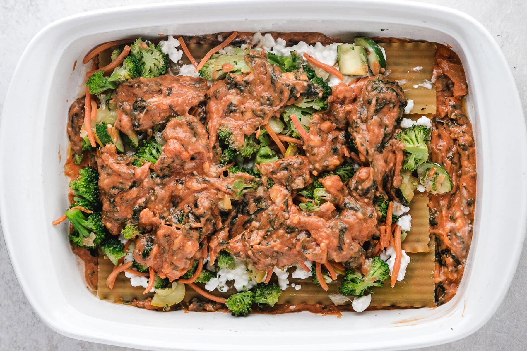 Vegetable mix being placed on top of cottage cheese layer, on top of lasagna noodles.