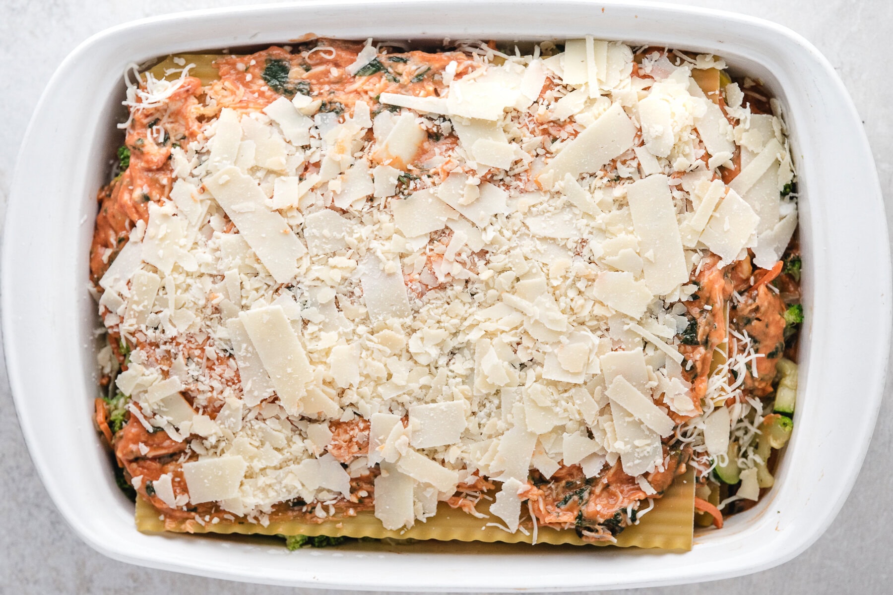 Layered veggie lasagna in baking dish, topped with cheese, ready to be baked