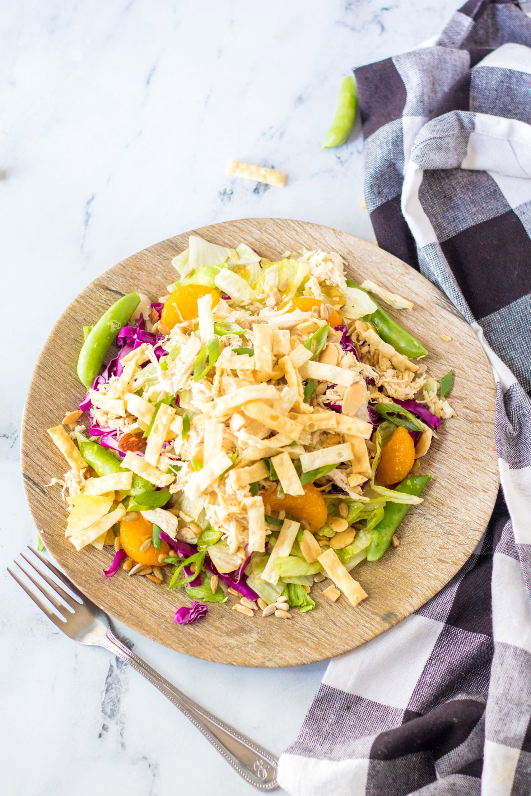 Chinese salad and dressing plated on a wooden plate with a fork to the side