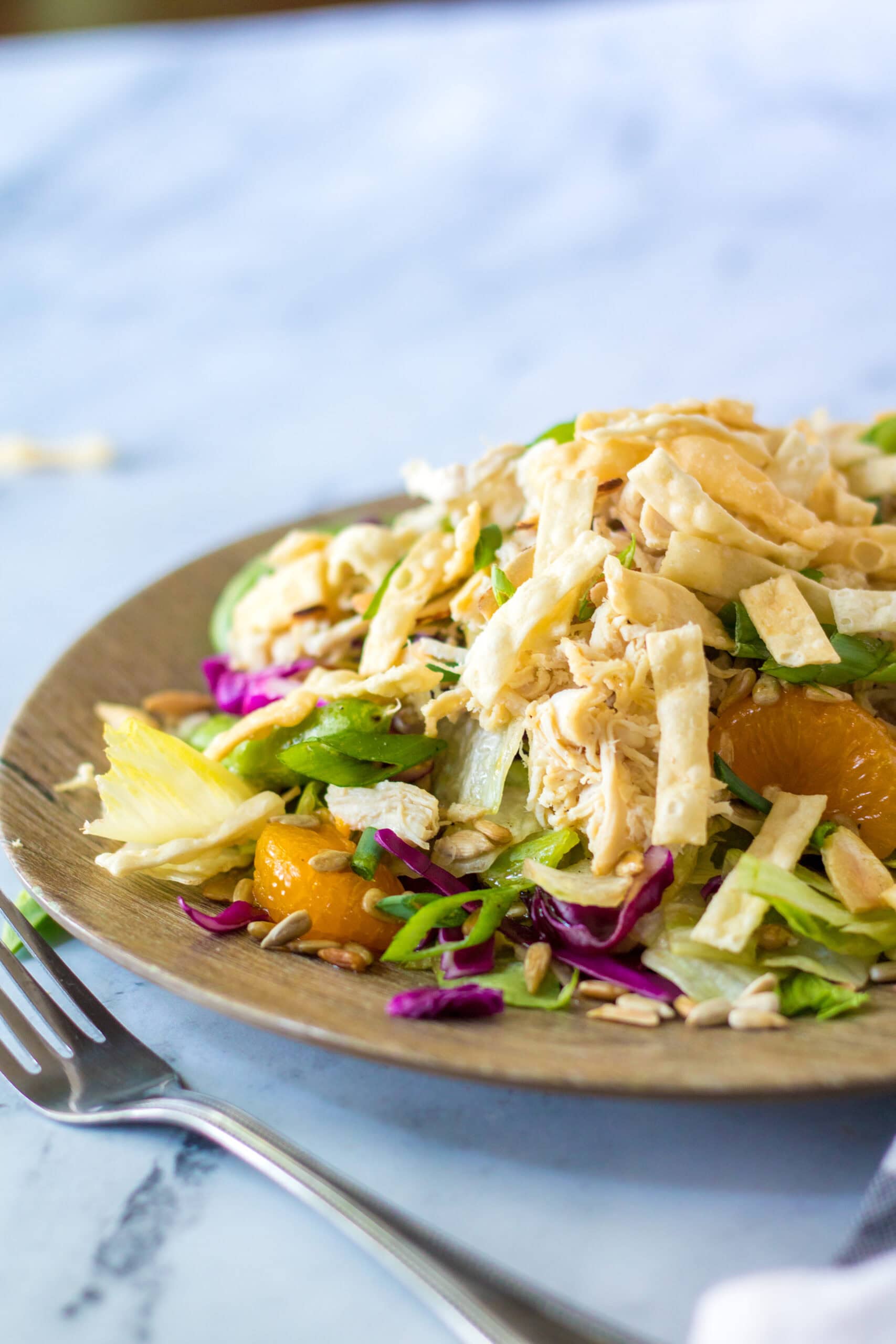 Chinese salad and dressing on a wooden plate with a fork to the side