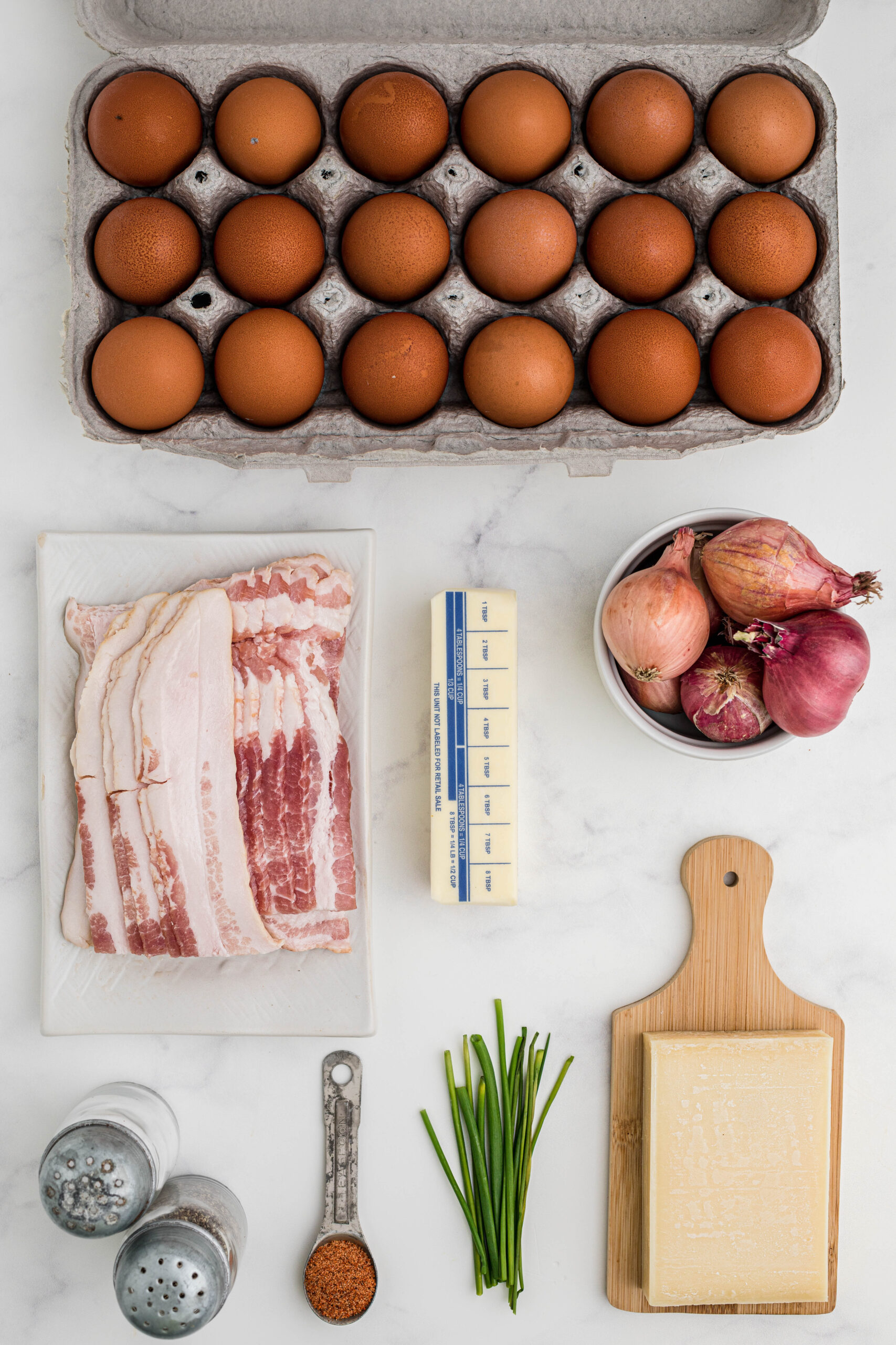 All ingredients to make breakfast muffins:eggs, bacon, shallots, butter, chives, gruyere cheese, cajun seasoning.