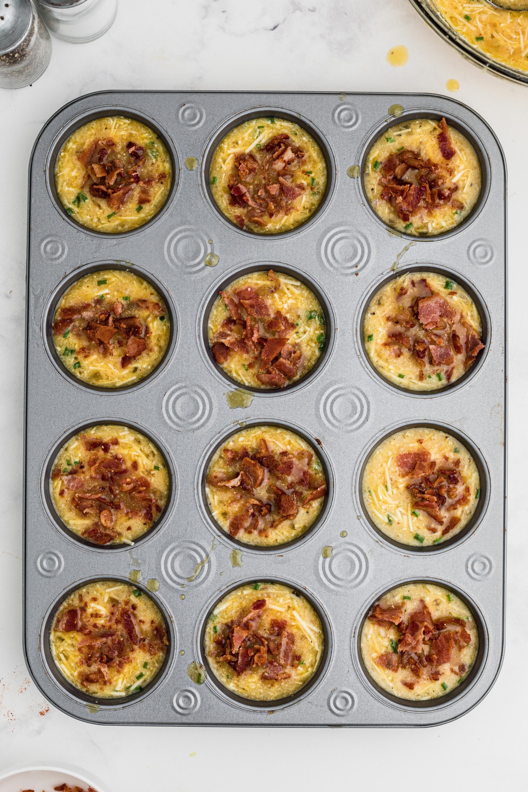 Bacon is being added to the tops of the breakfast muffins to finish the process of making the muffins