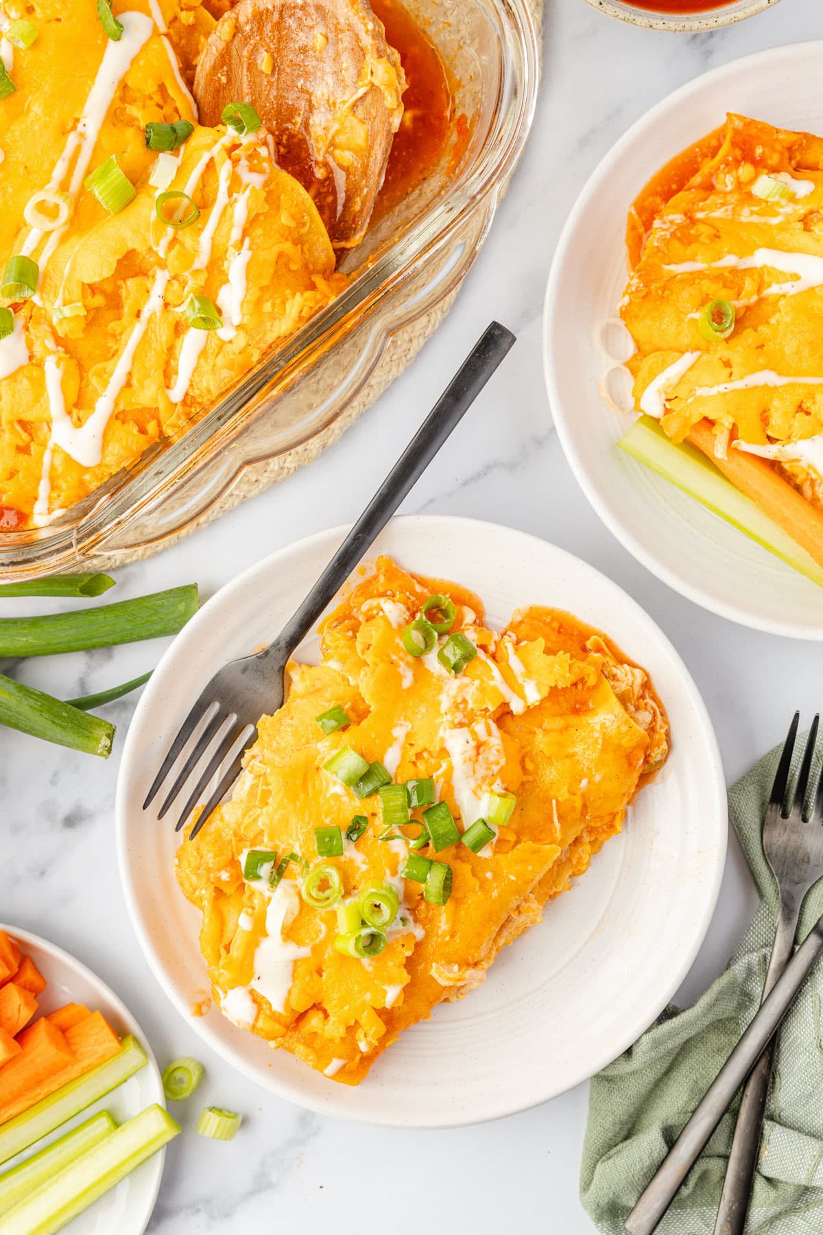 Plated buffalo chicken enchiladas with a fork, baking dish near by to grab more to enjoy