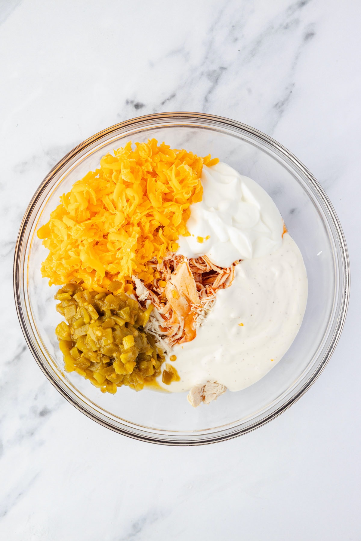 All ingredients to make the chicken mixture to place in tortillas: sour cream, shredded chicken, cheddar cheese, diced green chilis, hot sauce