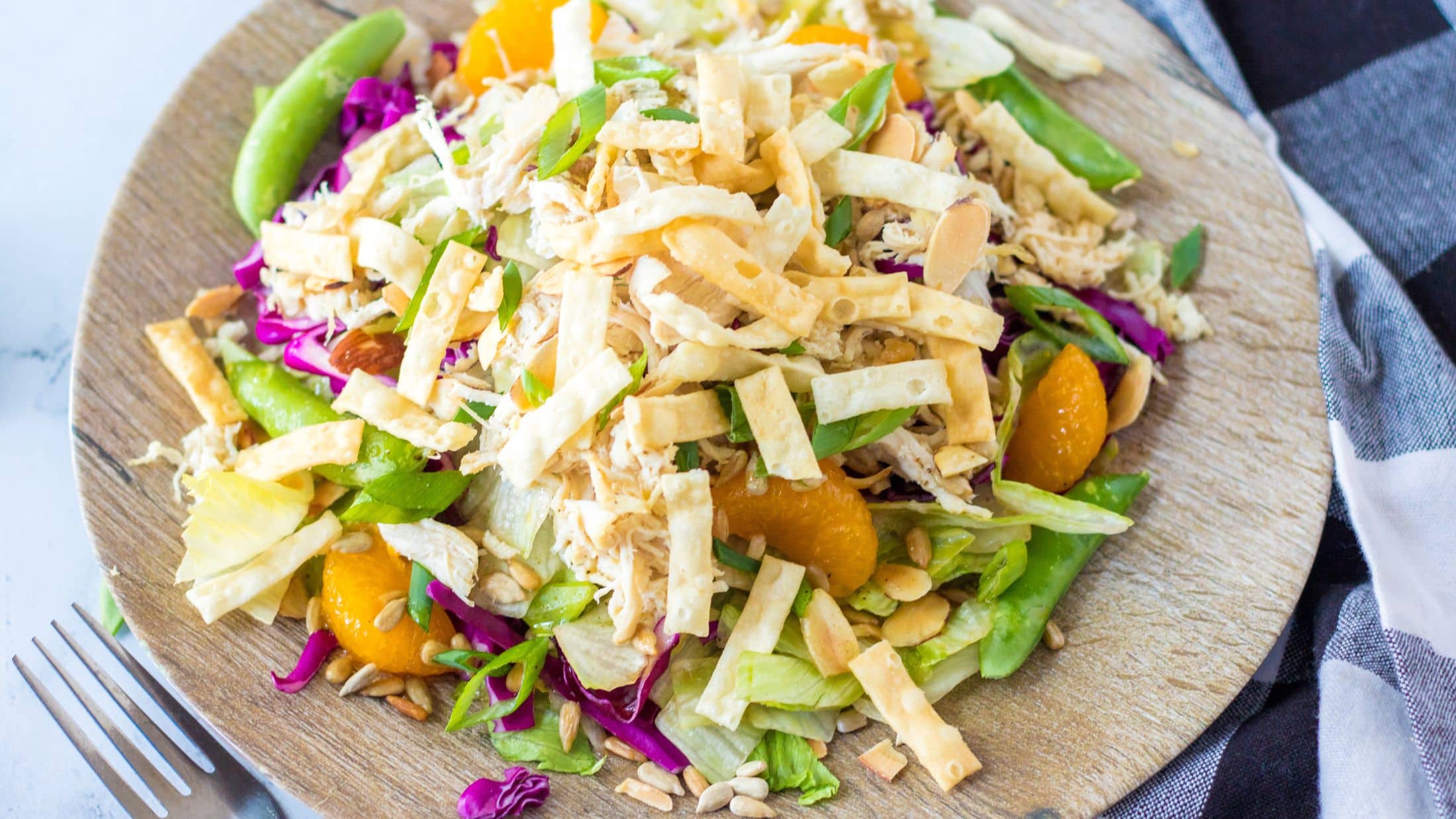 Chinese salad and dressing plated on a wooden plate, with a fork to the side