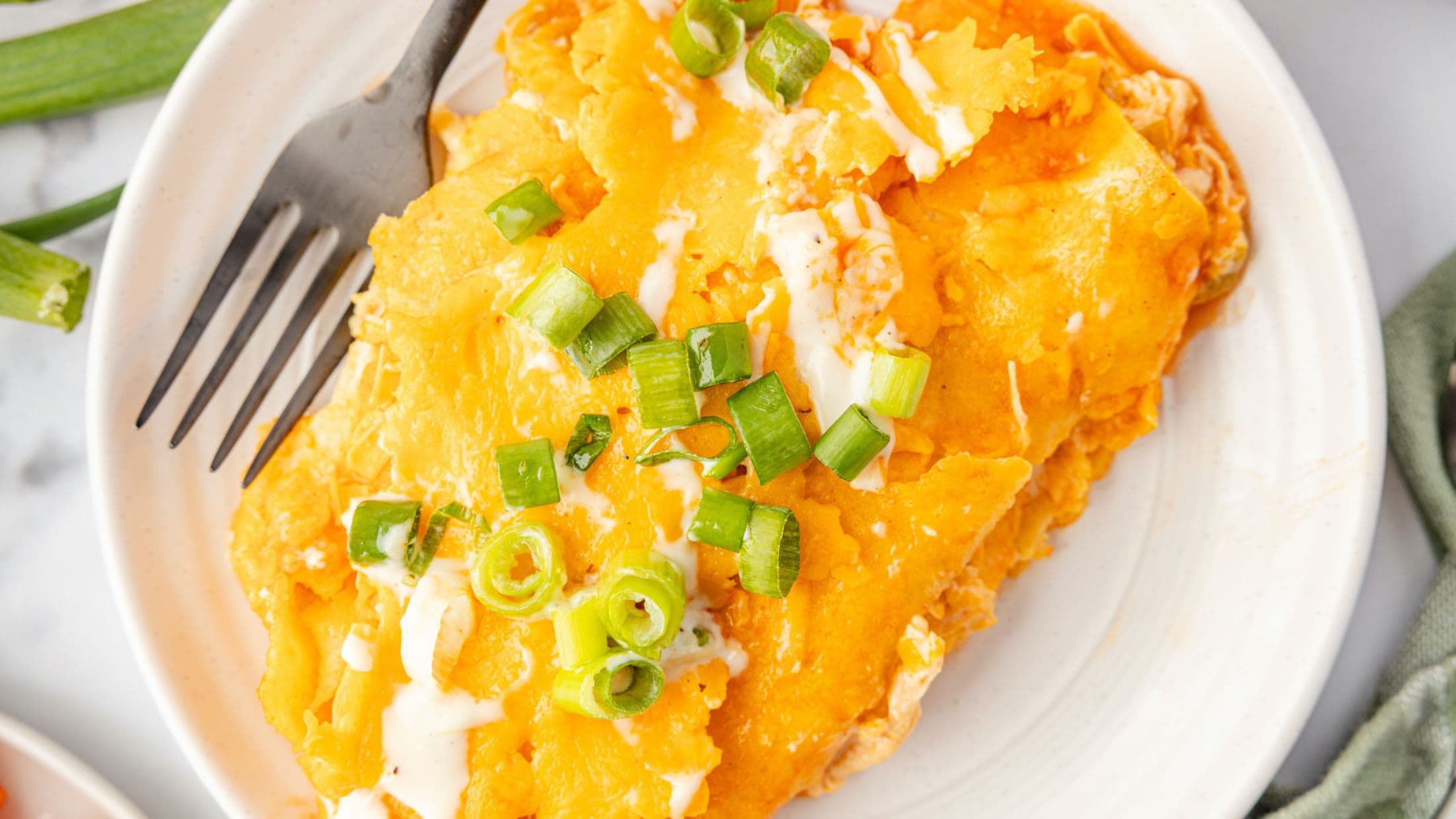 Two buffalo chicken enchiladas plated with a fork next to it, ready to be enjoyed