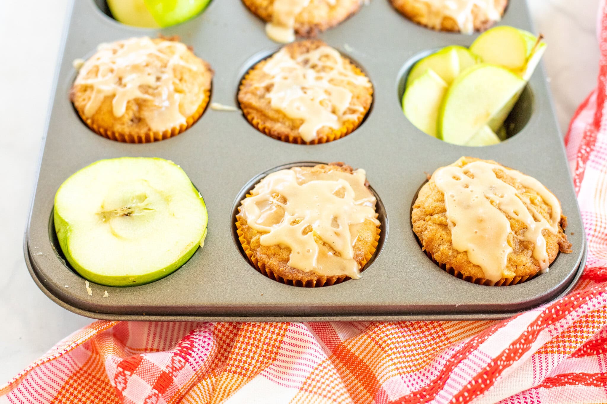 Caramel apple muffins with caramel drizzle in muffin tin ready to be plated.