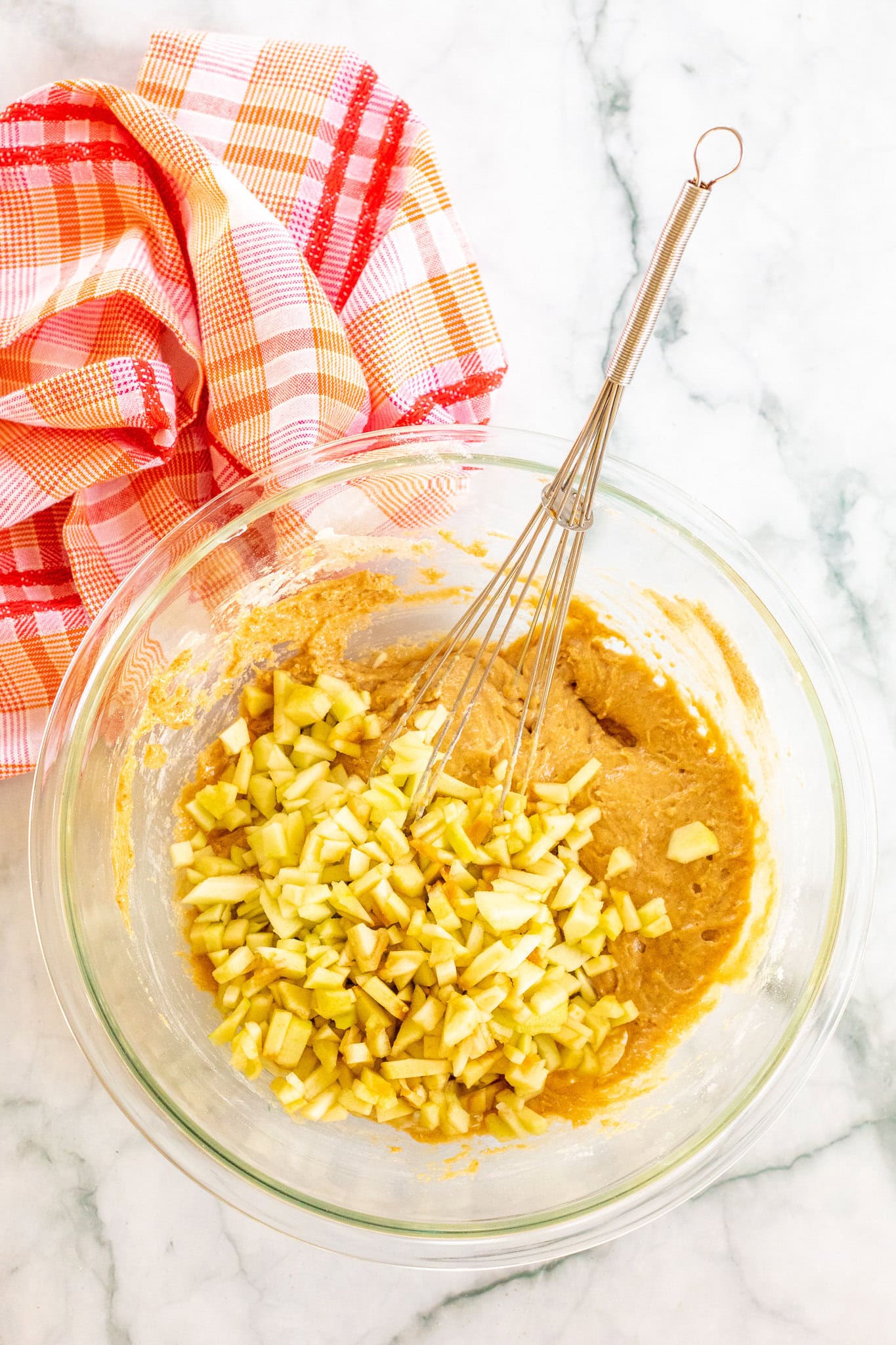 Caramel apple muffin batter in a mixing bowl with tossed in fresh apples