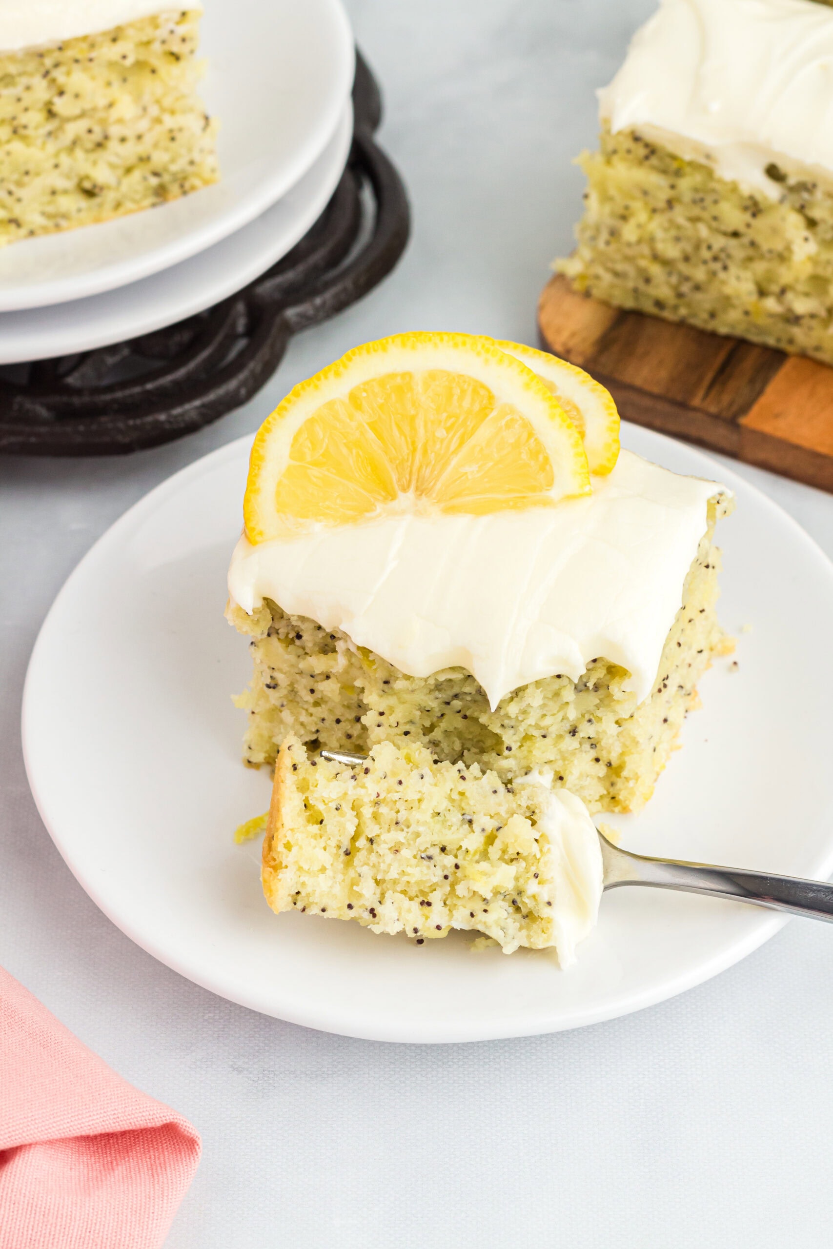 A square sliced of lemon poppy seed cake, and a fork is holding a bite size piece of the cake