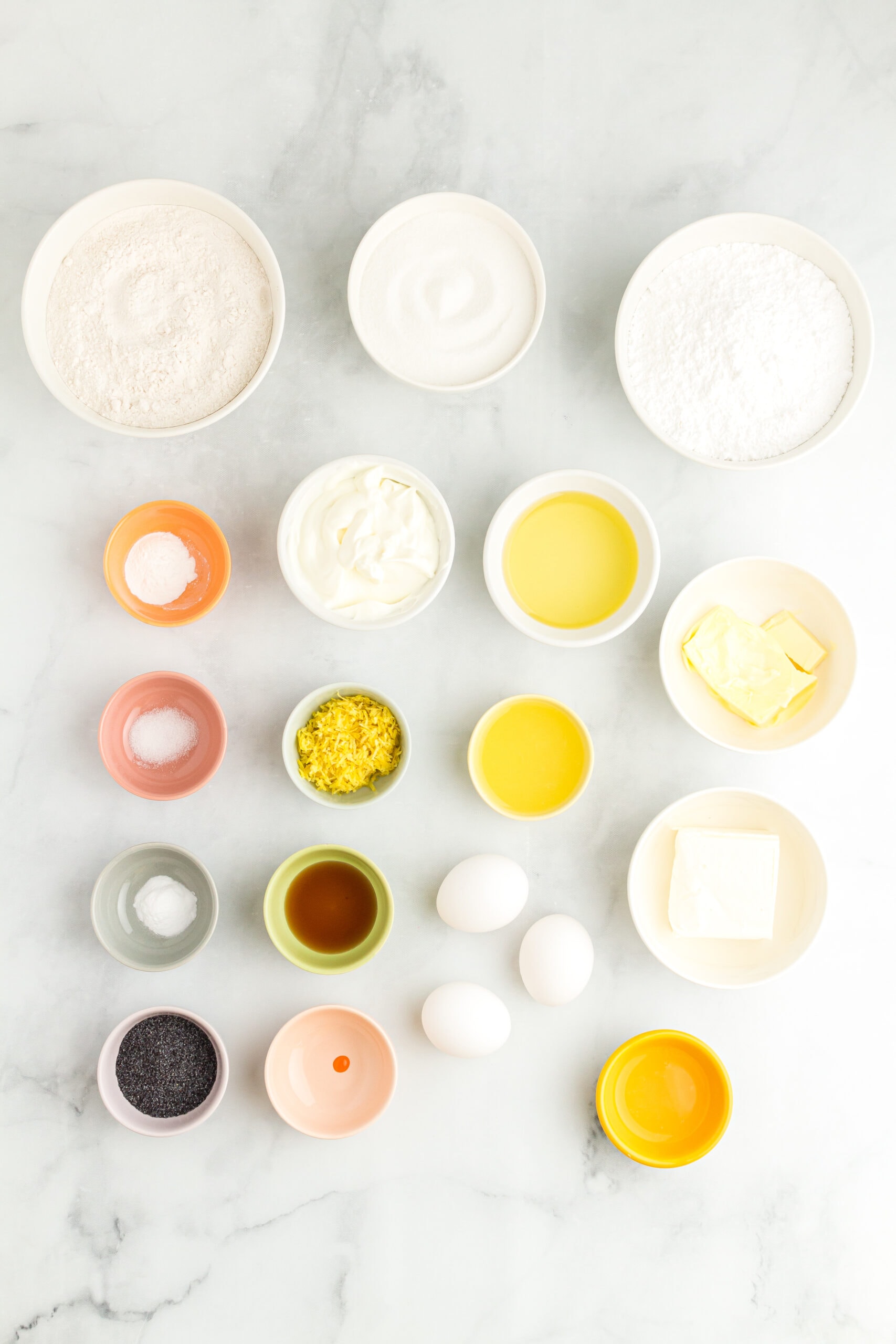 Ingredients to make the lemon poppy seed cake and frosting: flour, poppyseeds, baking powder & soda, salt, sugar, sour cream, vegetable oil, eggs, lemon zest, lemon juice, vanilla bean paste, yellow food coloring, powdered sugar, cream cheese, butter.