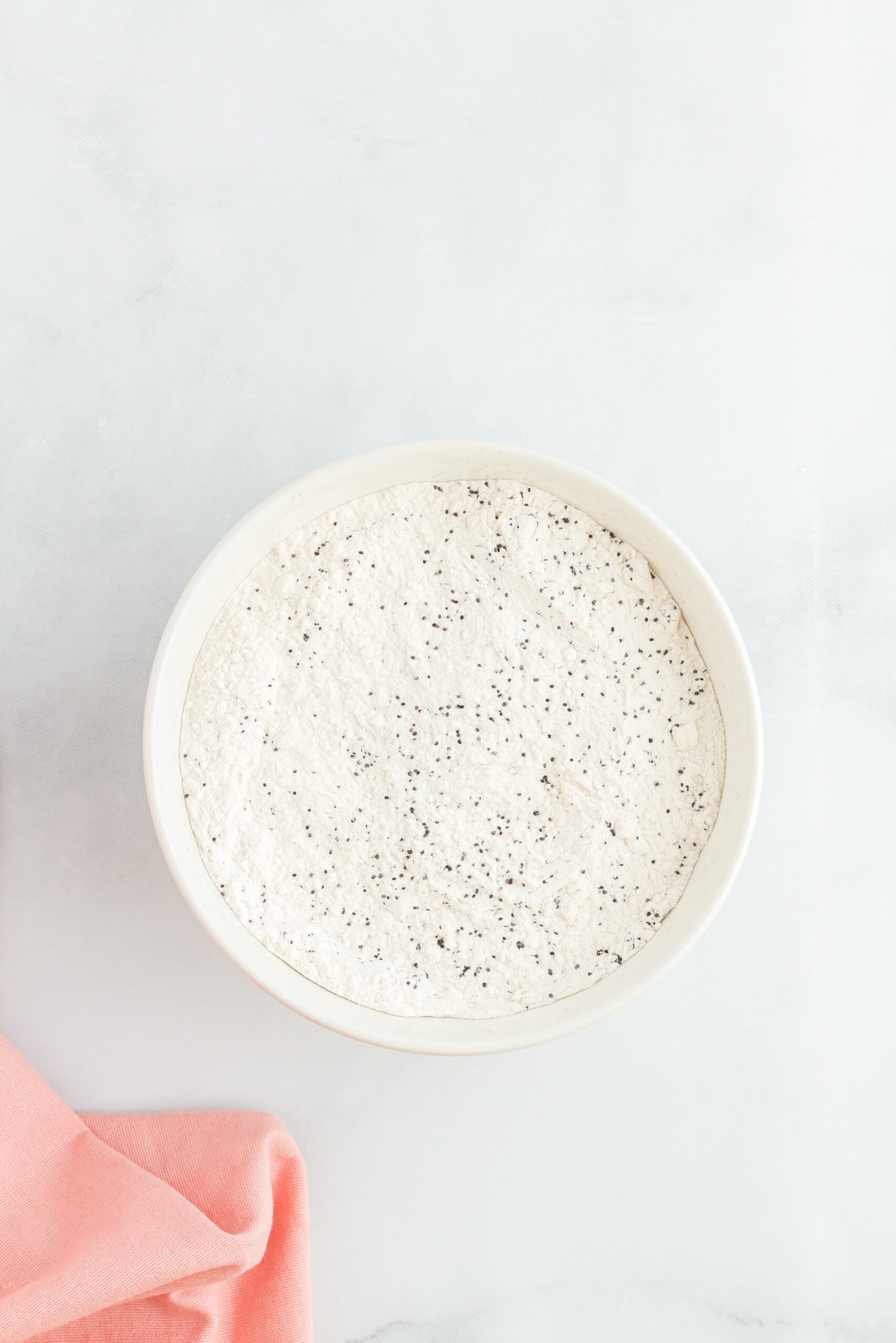 In a mixing bowl is flour, poppy seeds, baking powder, baking soda and salt.