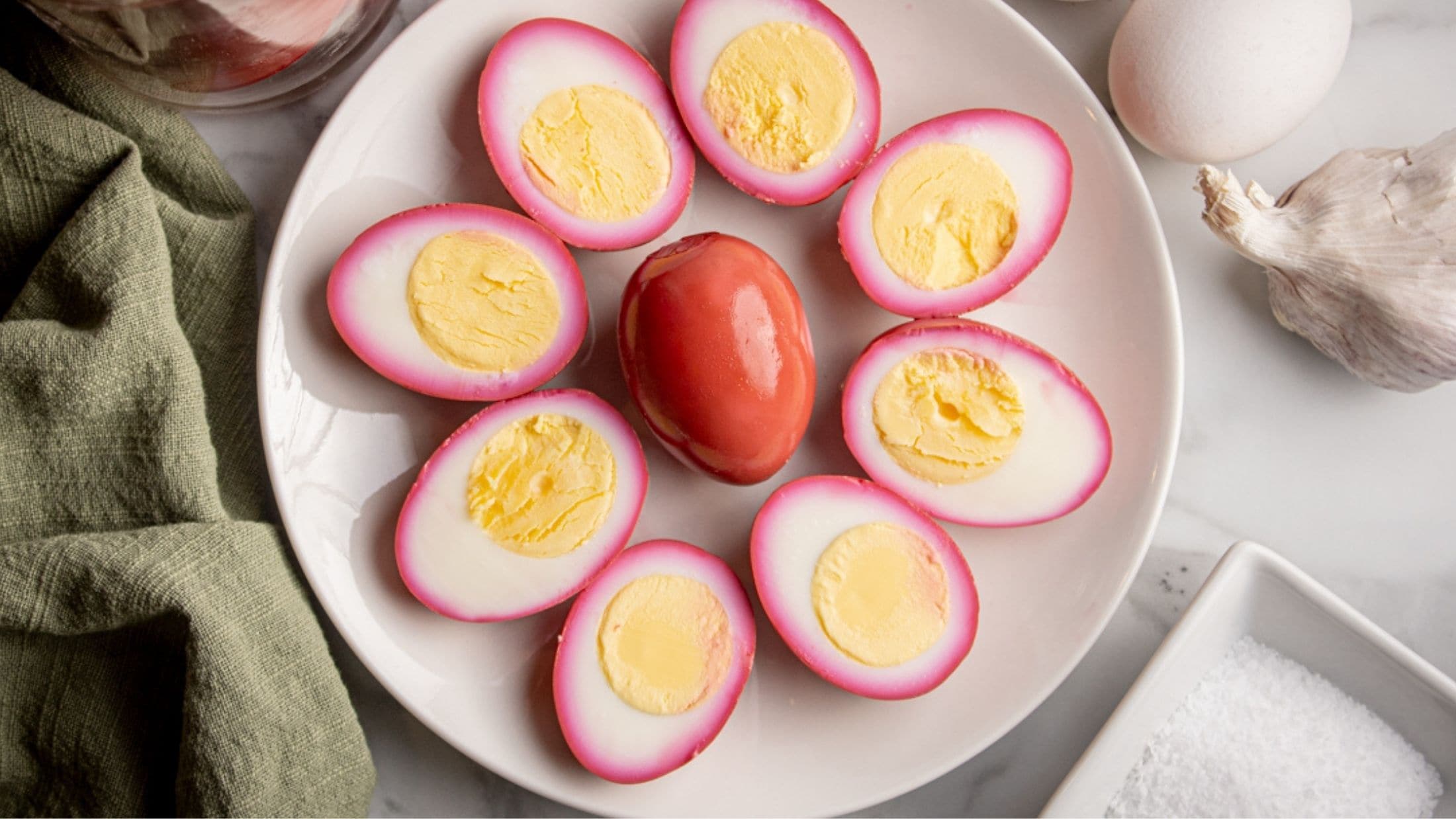 Pickled beet eggs all plated and the middle of the plate has a full egg and the full egg is surrounded by eggs cut in half