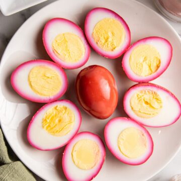 Pickled eggs on a plate, one in the middle is whole and the eggs surrounding it are cut up open to see the texture of the pickled egg