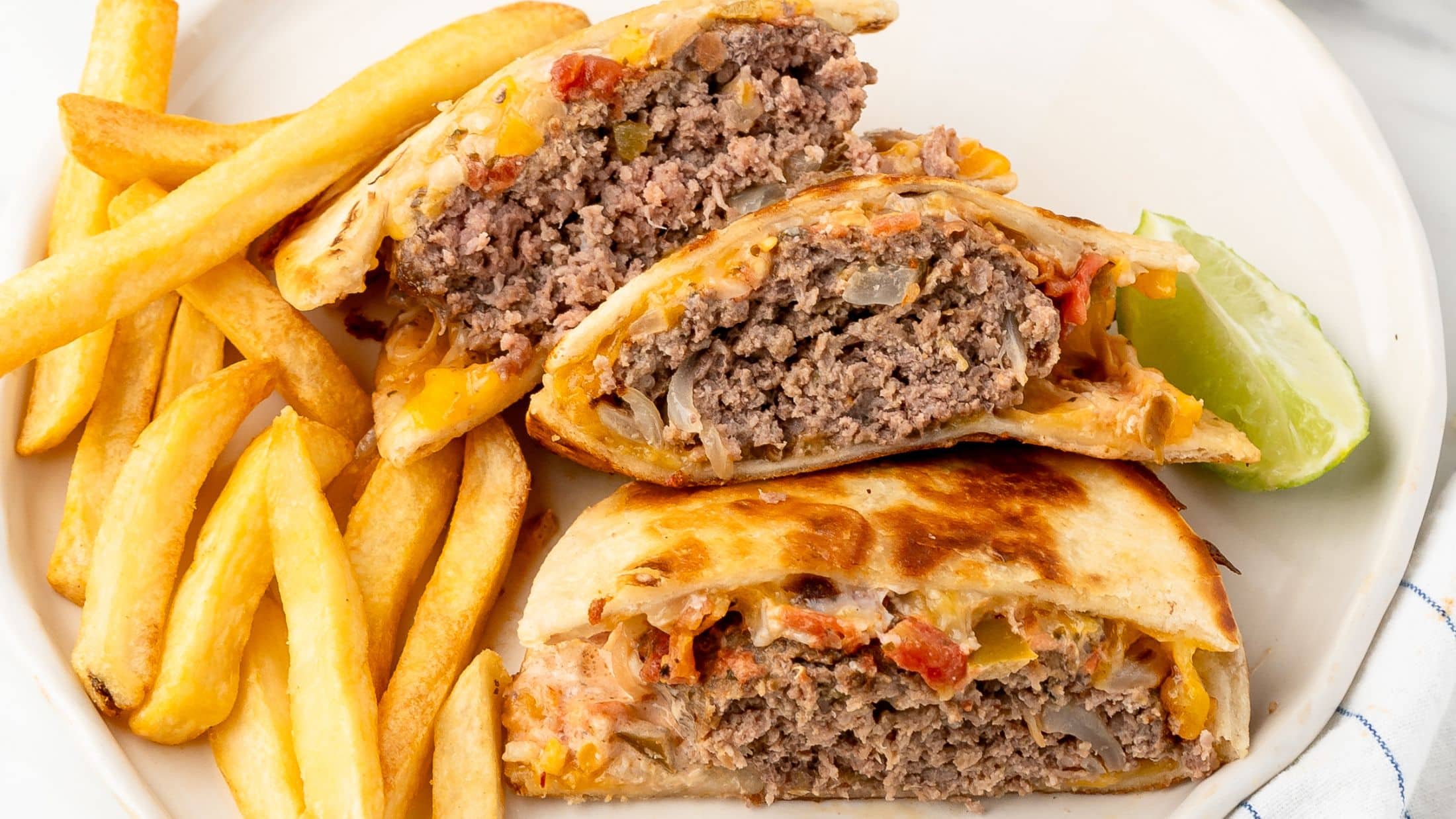 A stack of 3 quesadilla burger halves on a plate, with fries next to it