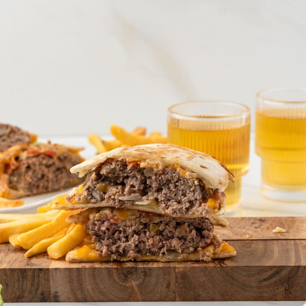 One quesadilla burger is cut in half, on a wooden board with fries on the side.