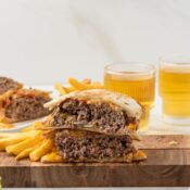 One quesadilla burger is cut in half, on a wooden board with fries on the side.