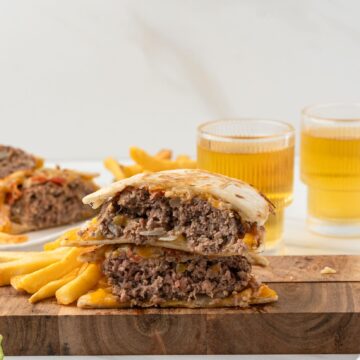 One quesadilla burger is cut in half, on a wooden board with fries on the side.