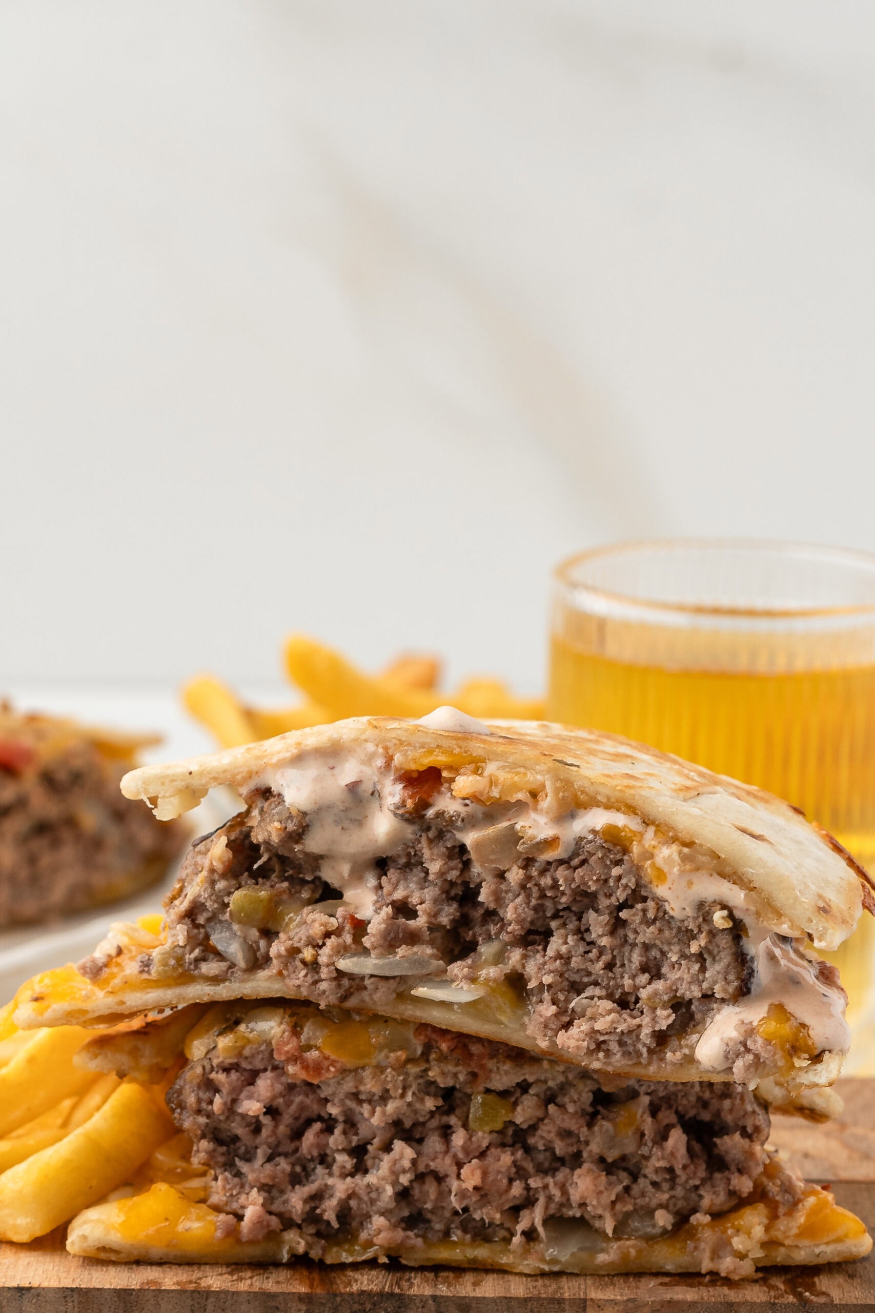 A quesadilla burger cut in half on a wooden cutting board with fries