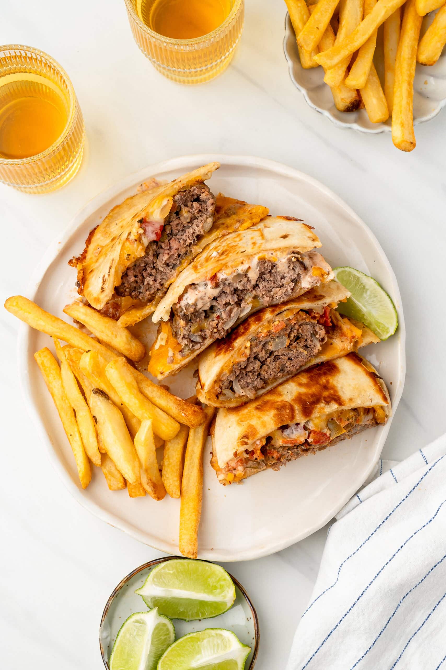 A stack of quesadilla burgers, fries on the side and lime wedges